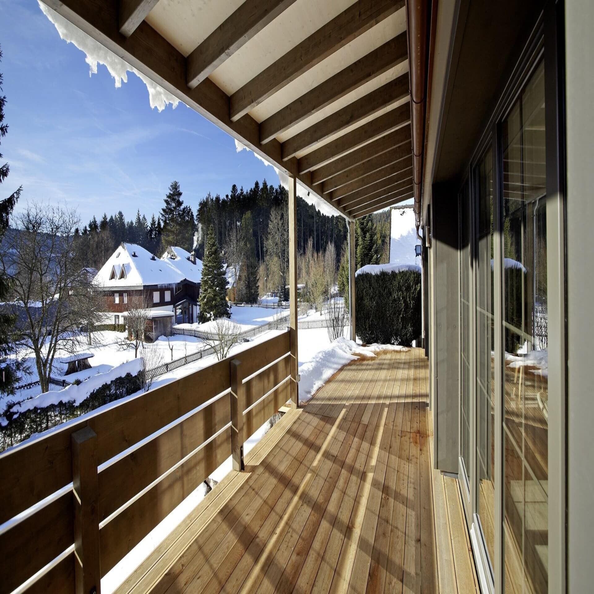 Überdachte Holzterrasse mit Blick auf die verschneite Landschaft.
