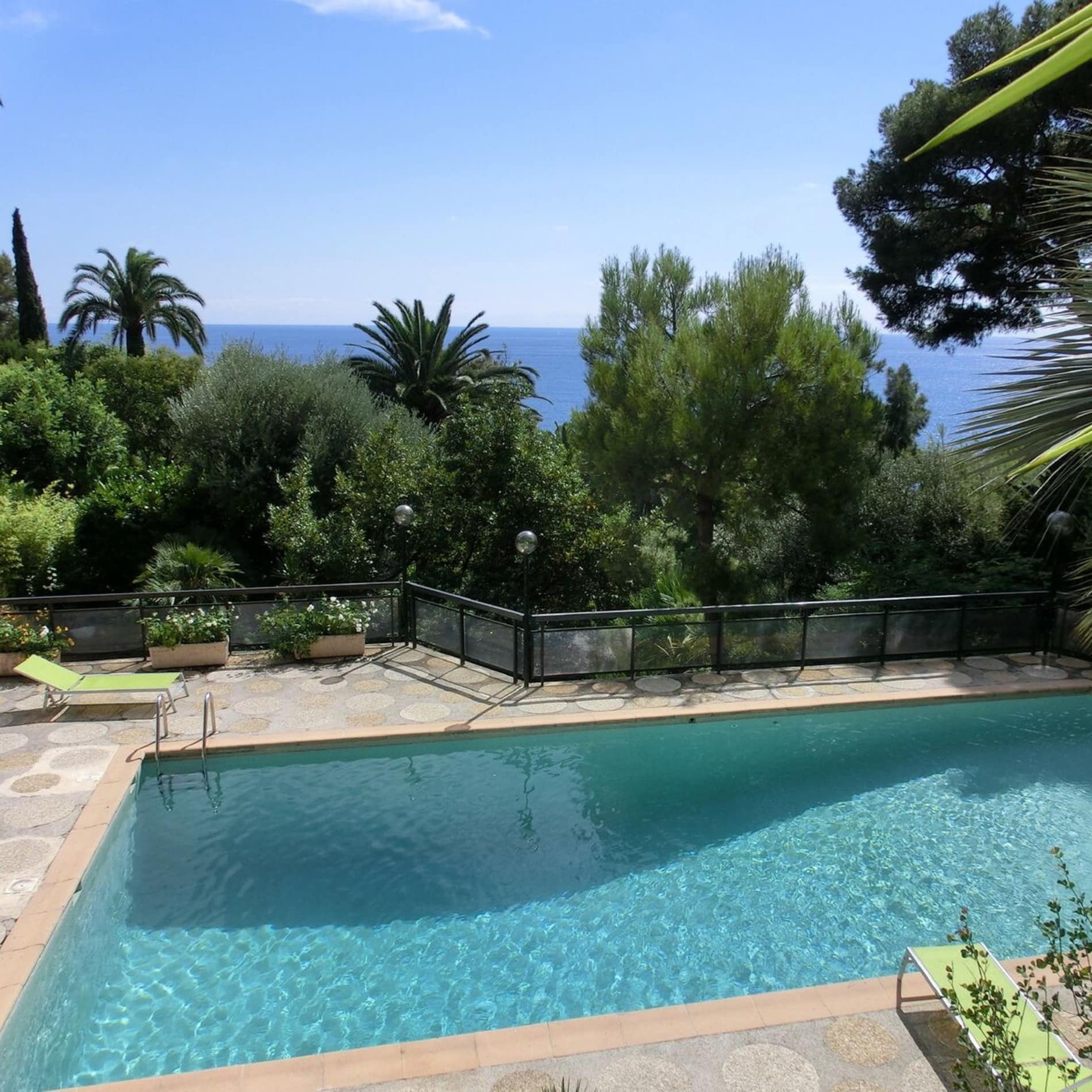 Ferienhaus in der Provence mit Pool, umgeben von Palmen und weiterem Grün, und Blick übers Meer
