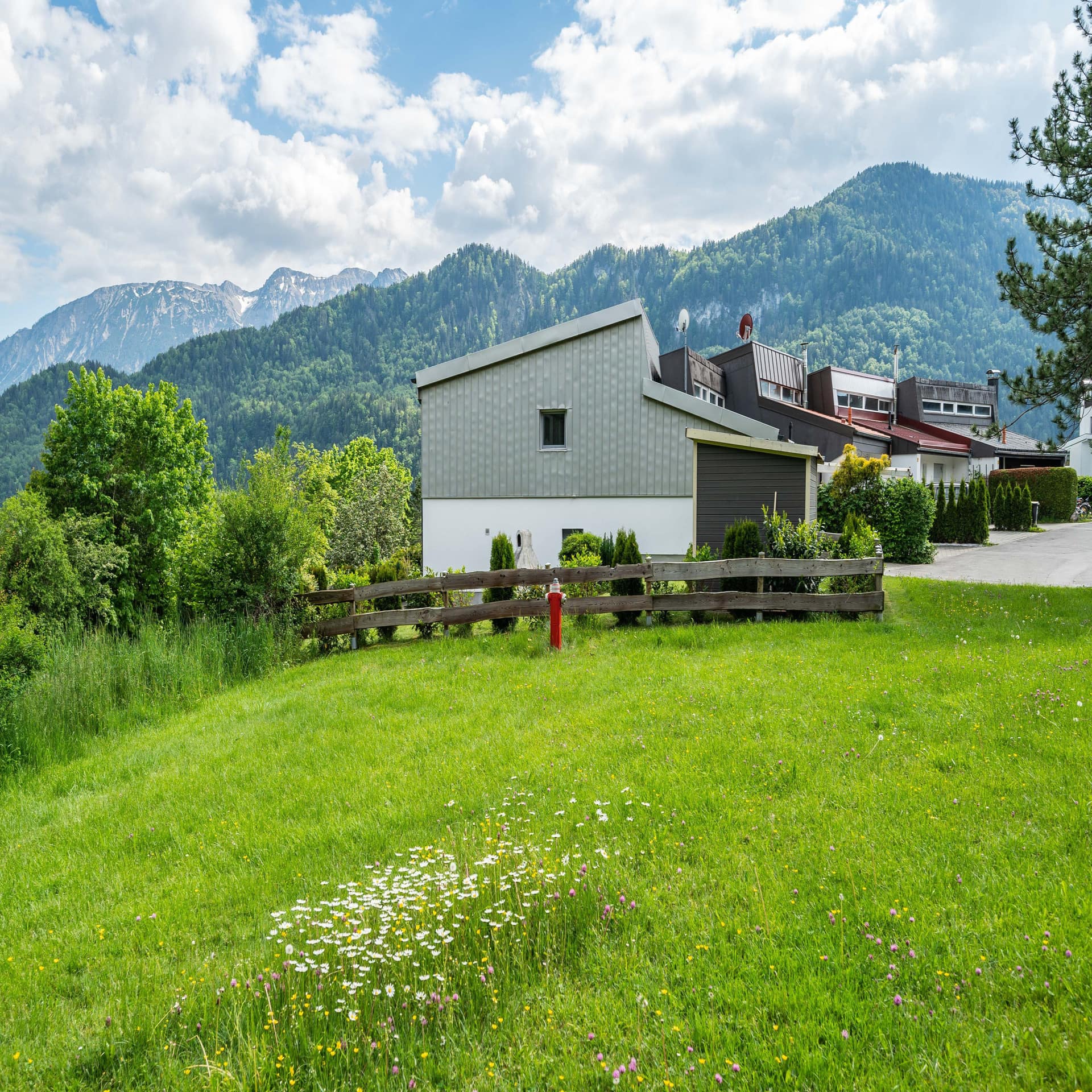 Eine grüne Wiese, dahinter Häuser und die bergige Landschaft.
