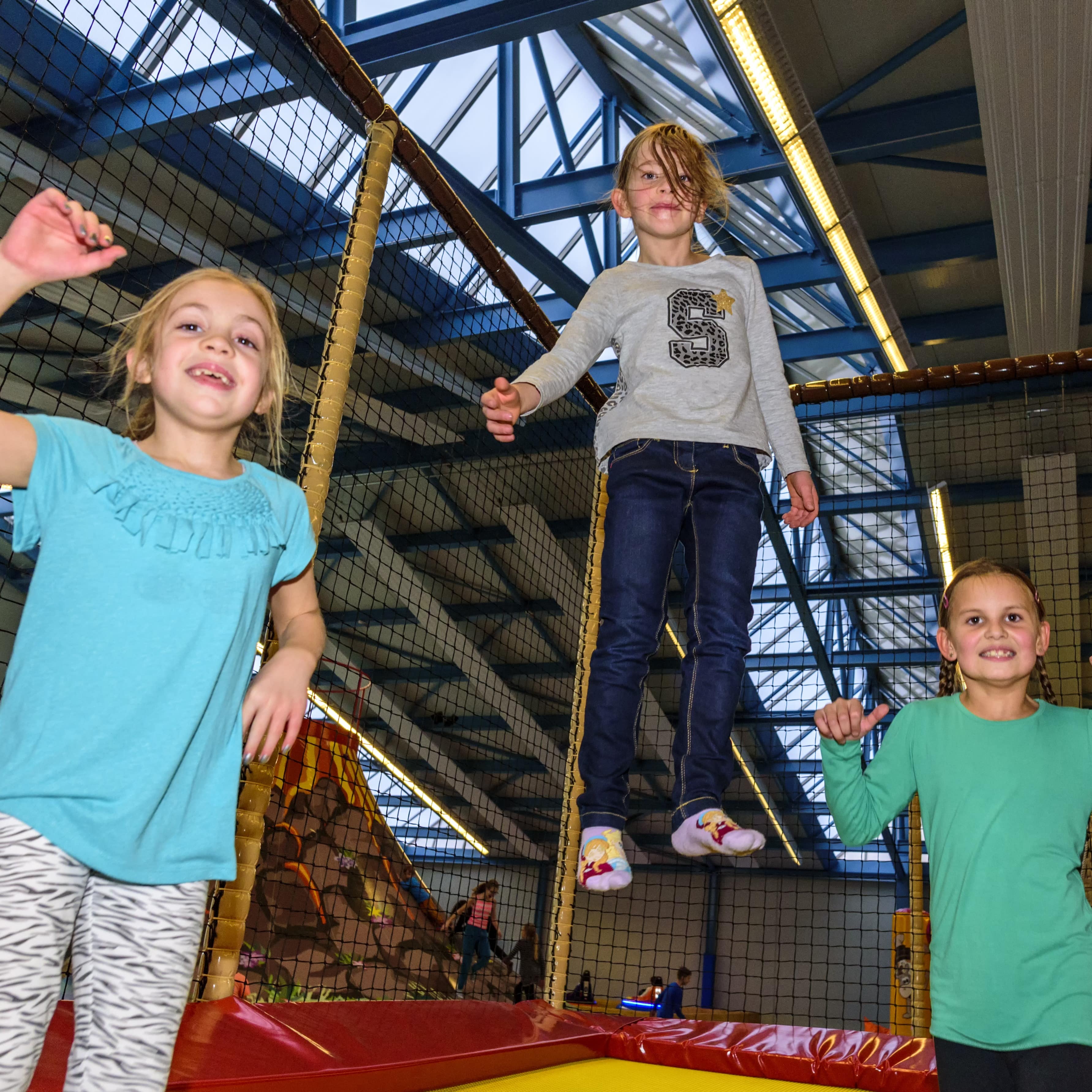 3 Mädchen hüpfen auf einem Trampolin in einer Trampolinhalle.
