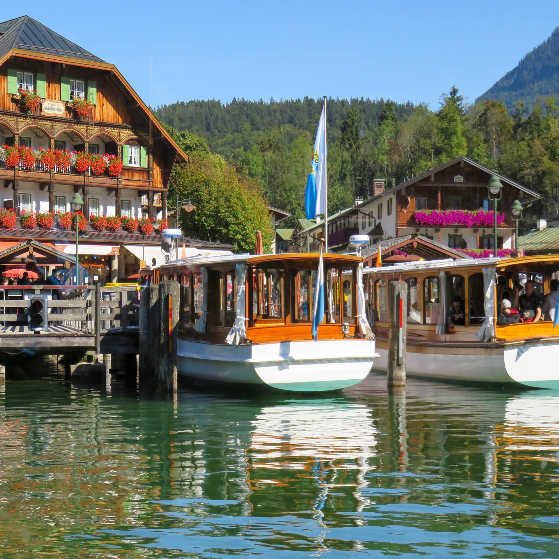 Urlauberboote vor bayerischer Dorfkulisse mit Wäldern im Hintergrund. 