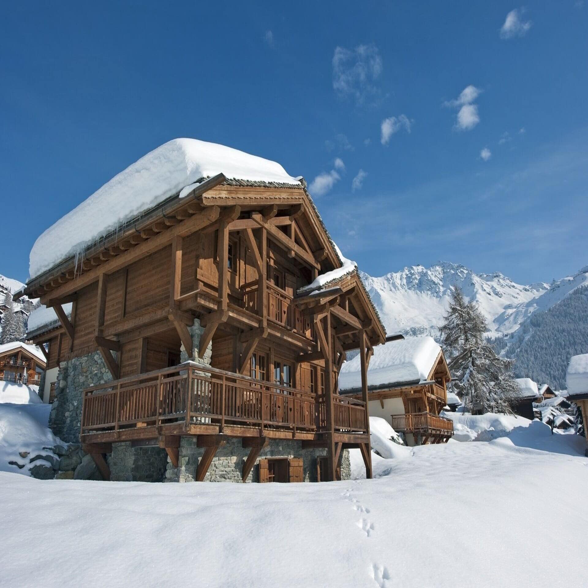 Verschneite Holzhäuser, im Hintergrund die Berge von Verbier.