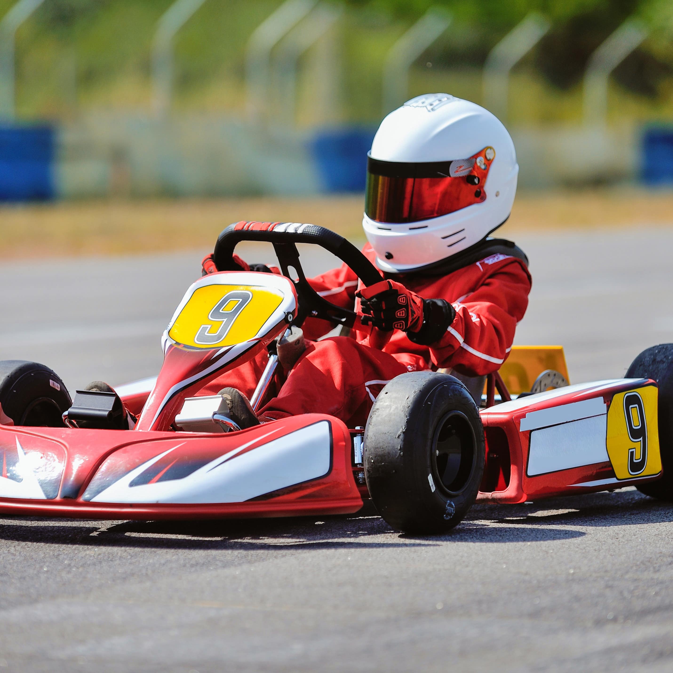 Kind in rotem Rennanzug mit weißem Helm in einem roten Gokart.