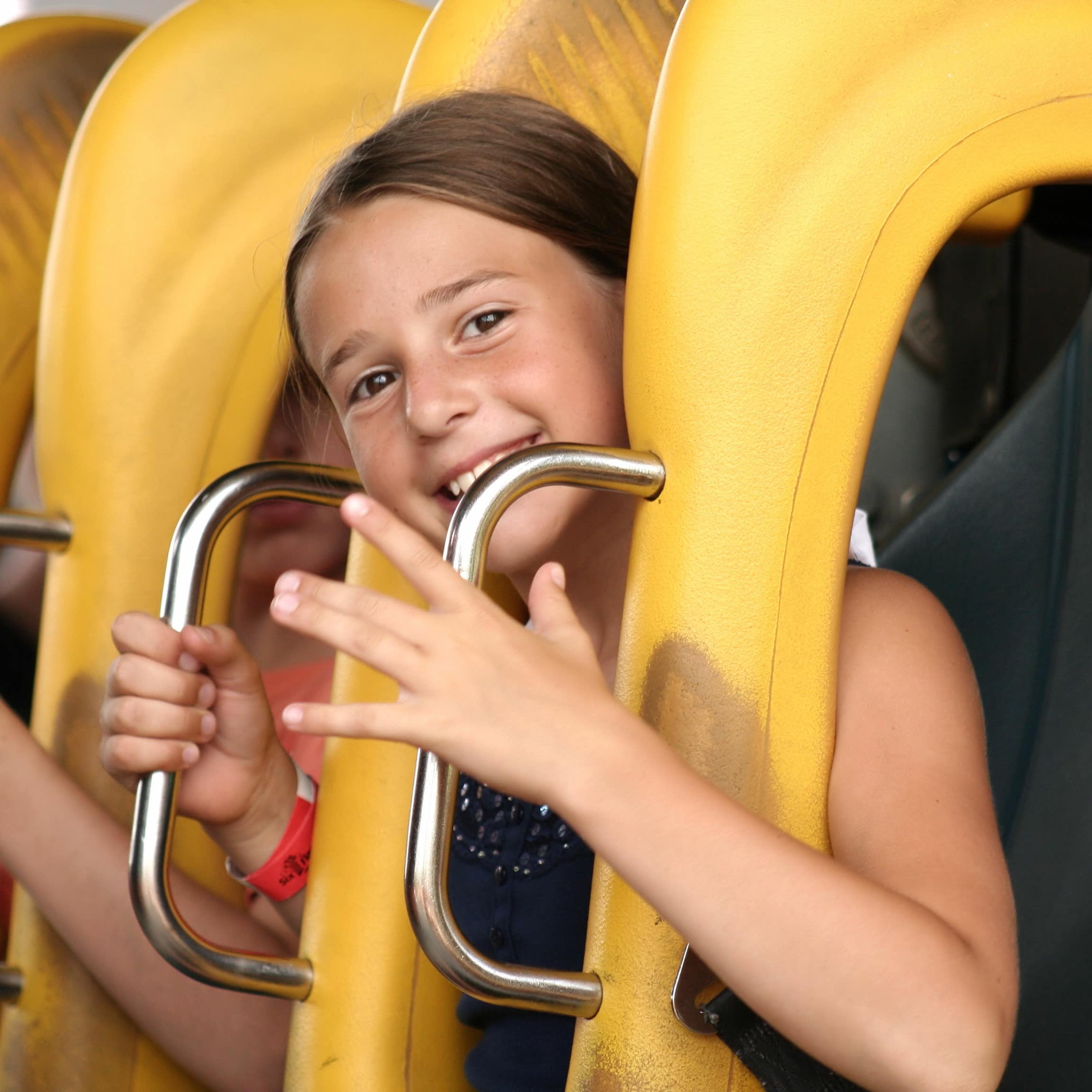 Nahaufnahme: Ein Mädchen in Sommerkleidung auf einem Achterbahnsitz hält sich an Griffen fest.