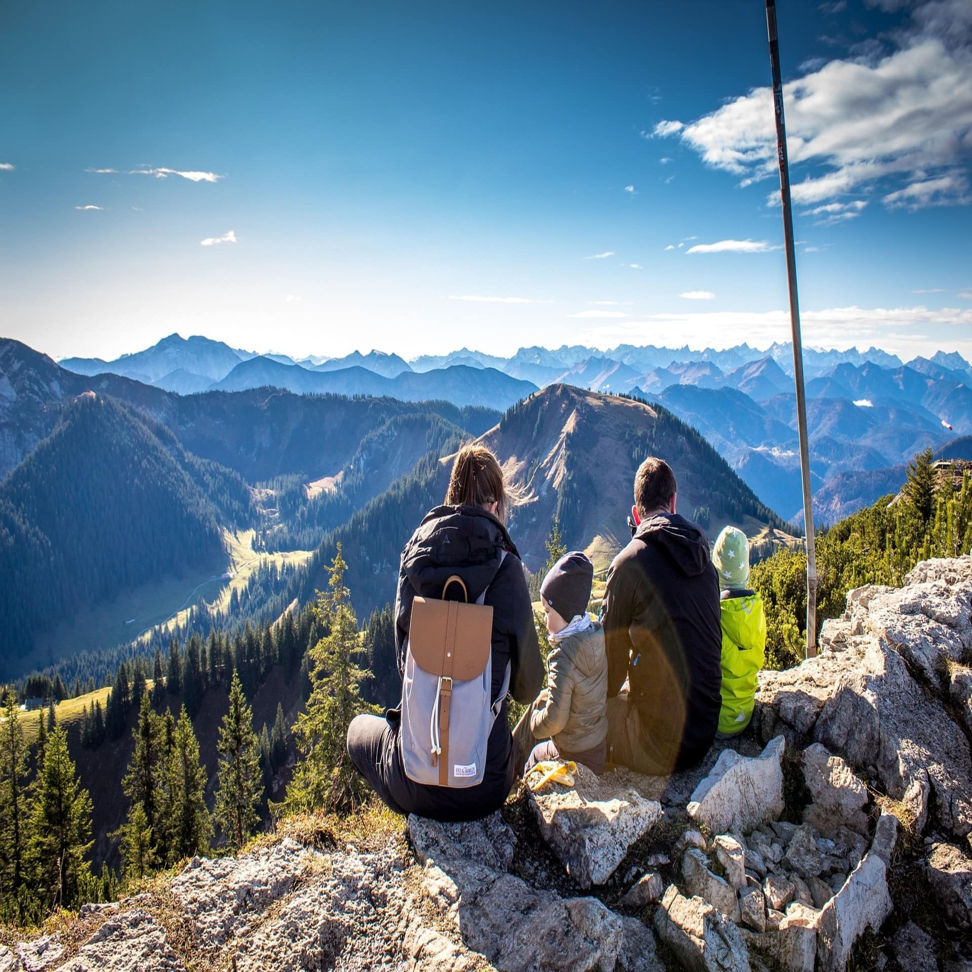 Eine Familie mit 2 Kindern sitzt auf einem Berg und blickt auf das Bergpanorama. 