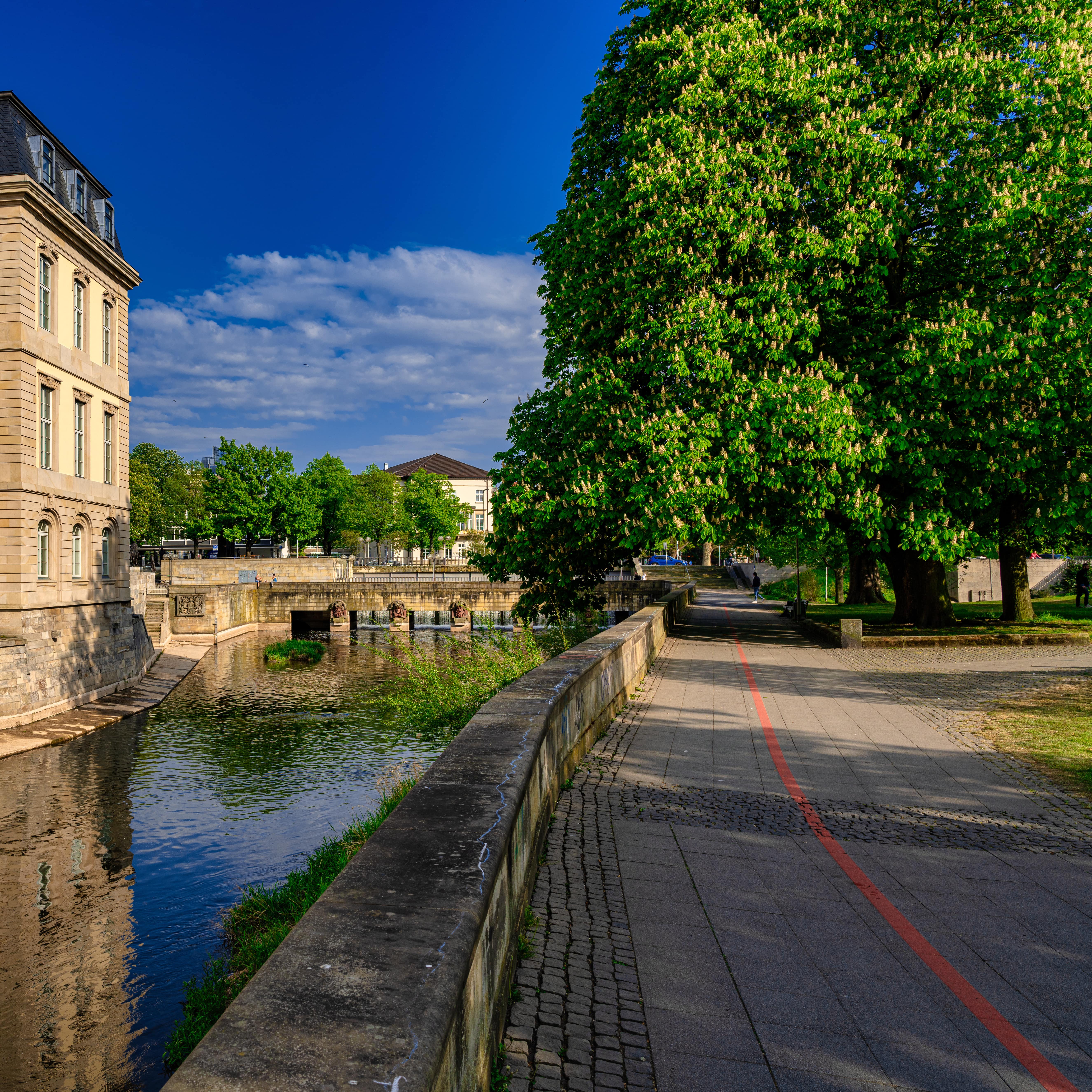 An der Promenade am Flussufer verläuft der Rote faden, links der Fluss und der Landtag.