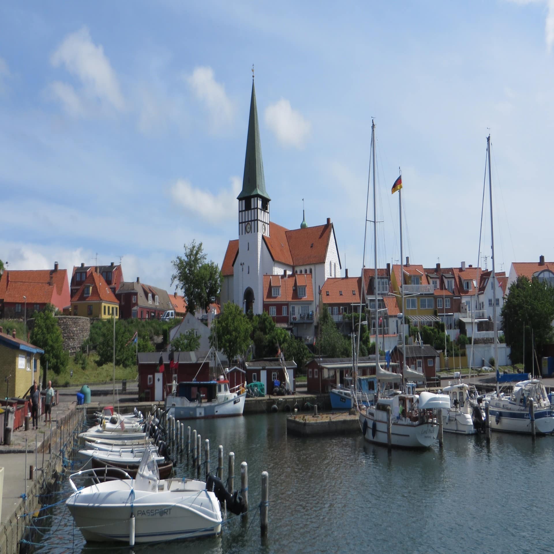 Blick über den Hafen von Rønne mit kleinen Booten, dahinter Häuser und eine Kirche.