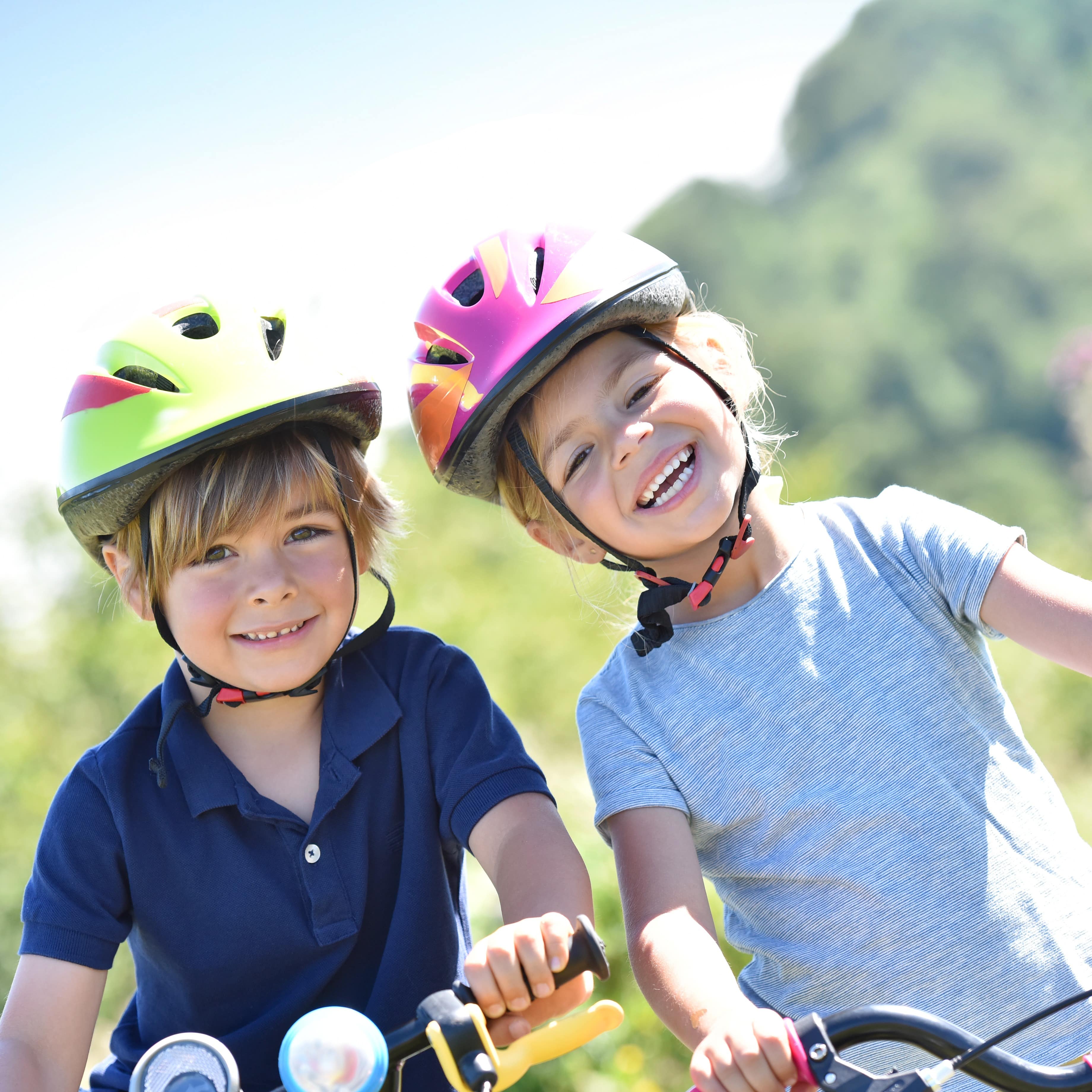 2 Kinder mit Fahrradhelmen auf Fahrädern lachen in die Kamera.