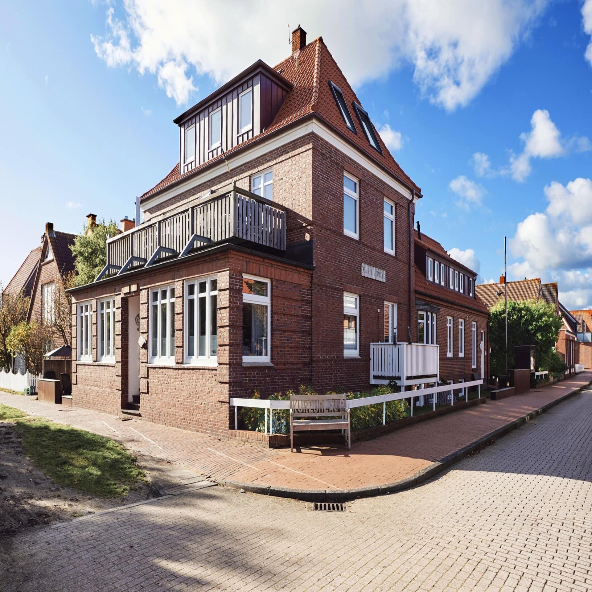 Rotes Friesenhaus mit Sitzbank im Zentrum von Juist, die Sonne scheint, der Himmel ist blau. 