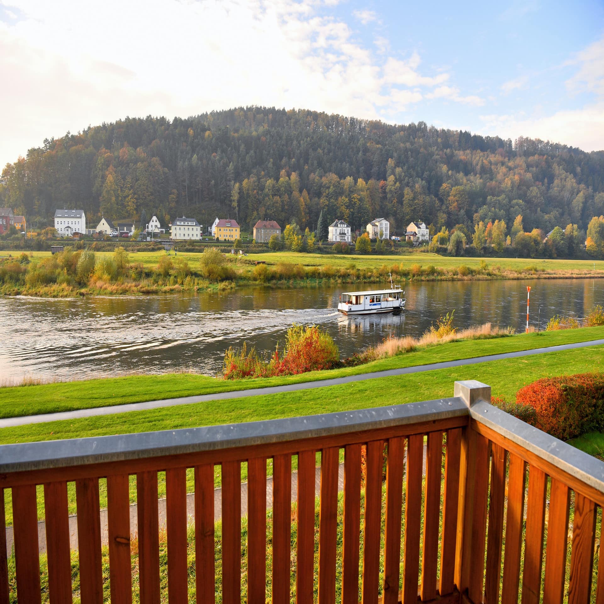 Blick vom Balkon auf die Elbe auf der ein Boot fährt und das gegenüberliegende Ufer mit Häusern und Wald.