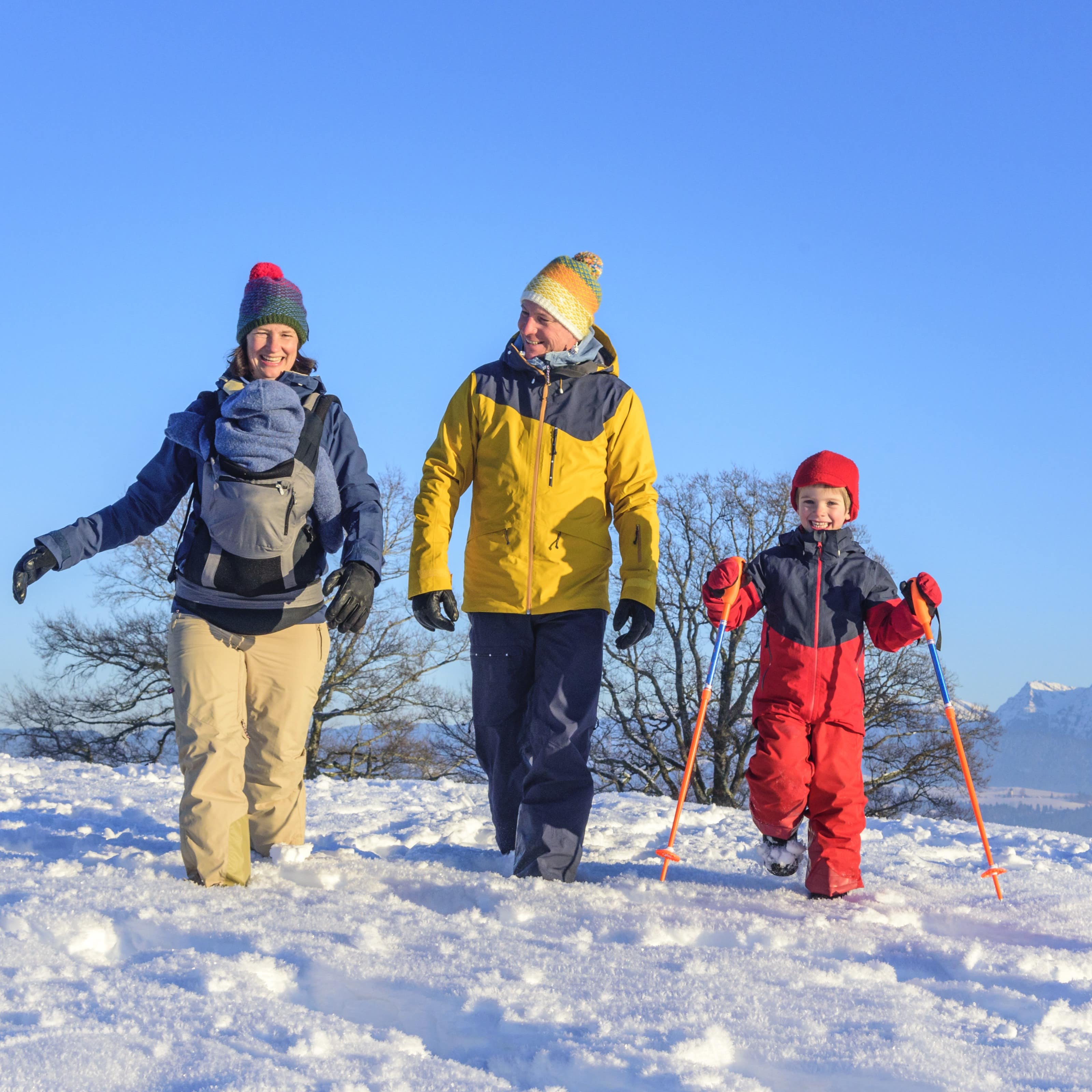 Familie mit Kind wandert durch den Schnee, die Mutter trägt ein Baby.