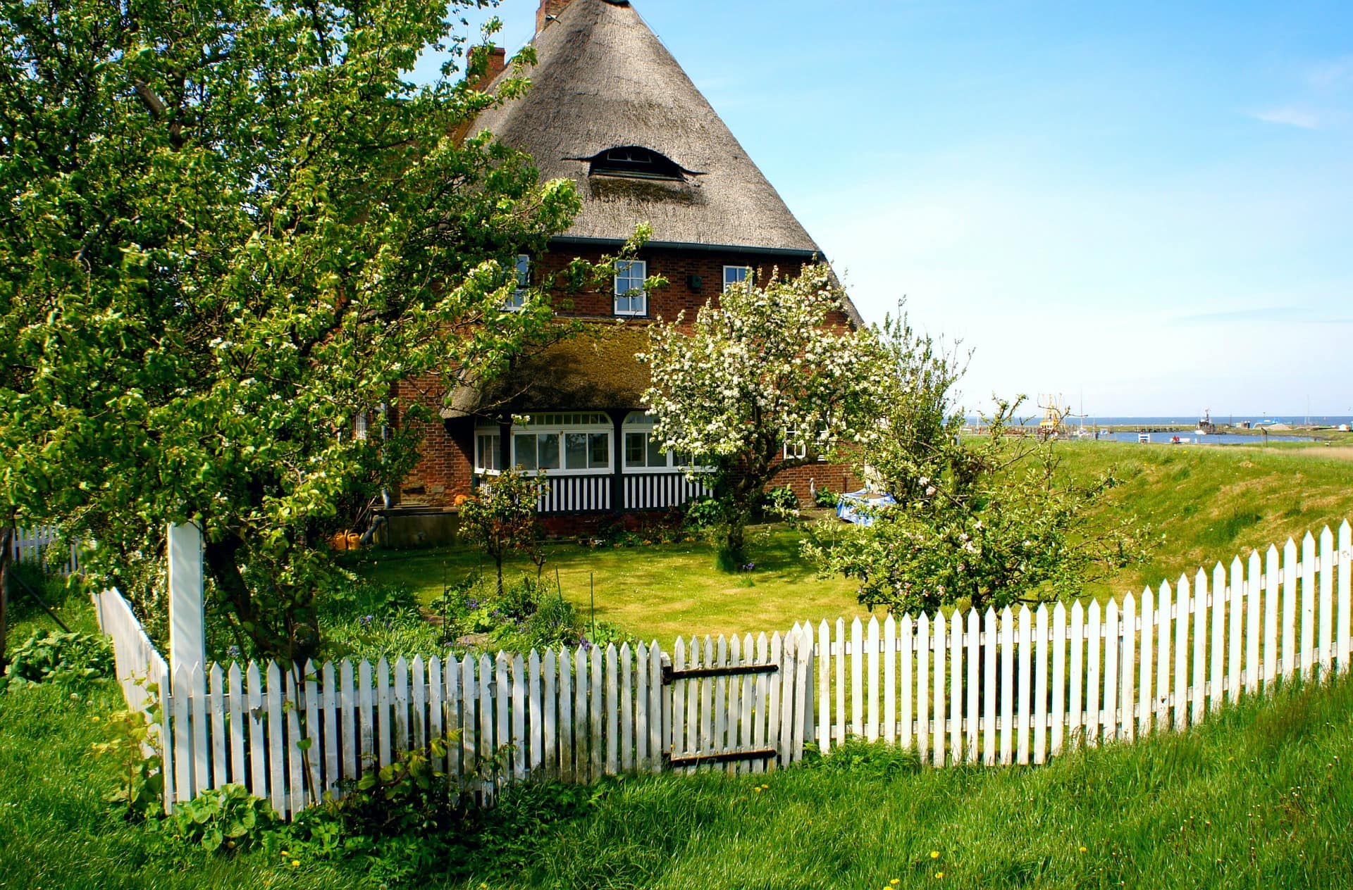 Ein traditionelles Haus mit Garten umgeben von einem weißen Zaun liegt direkt am Wasser