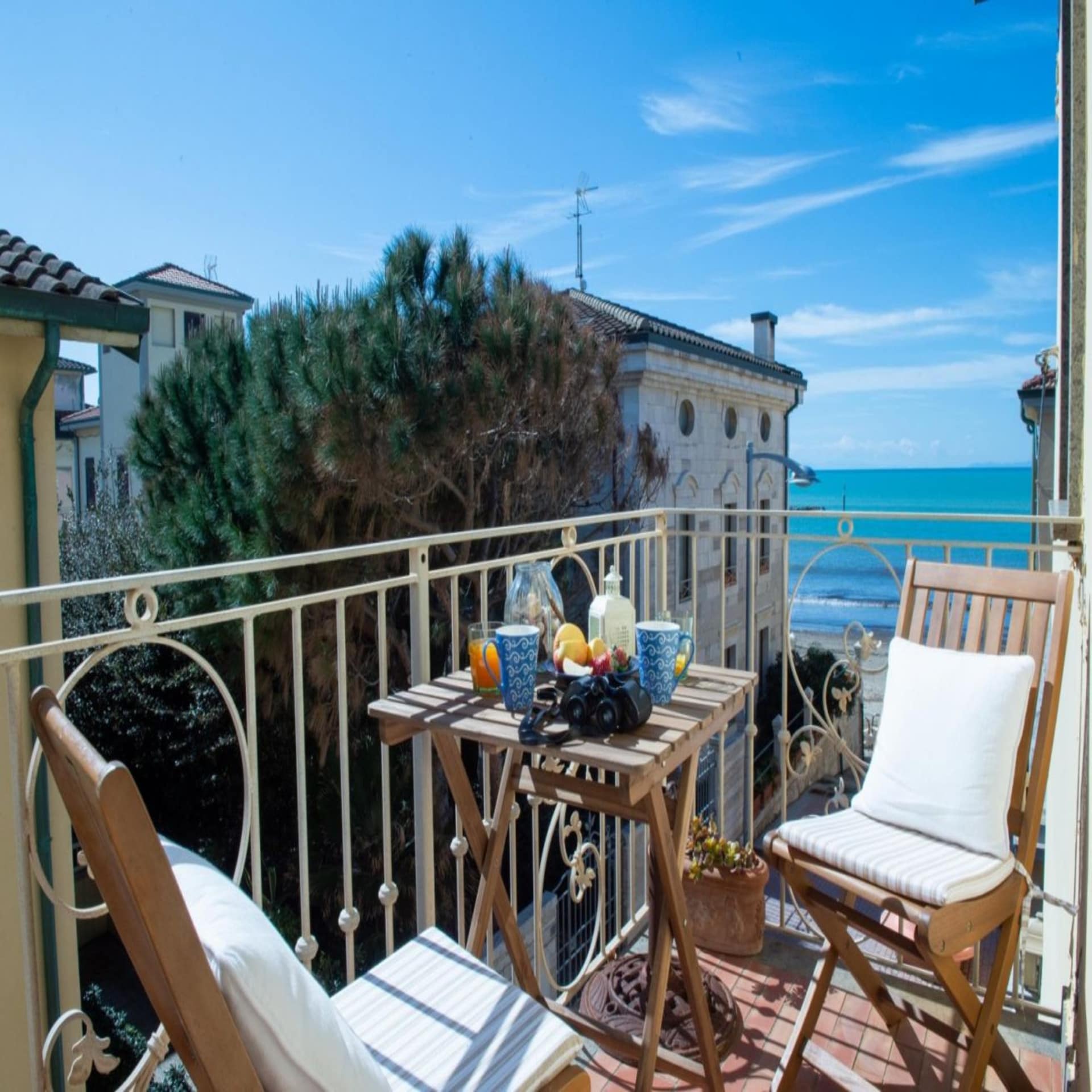 Kleiner Balkon mit Frühstückstisch für 2 und Blick auf das Meer. Die Sonne scheint.