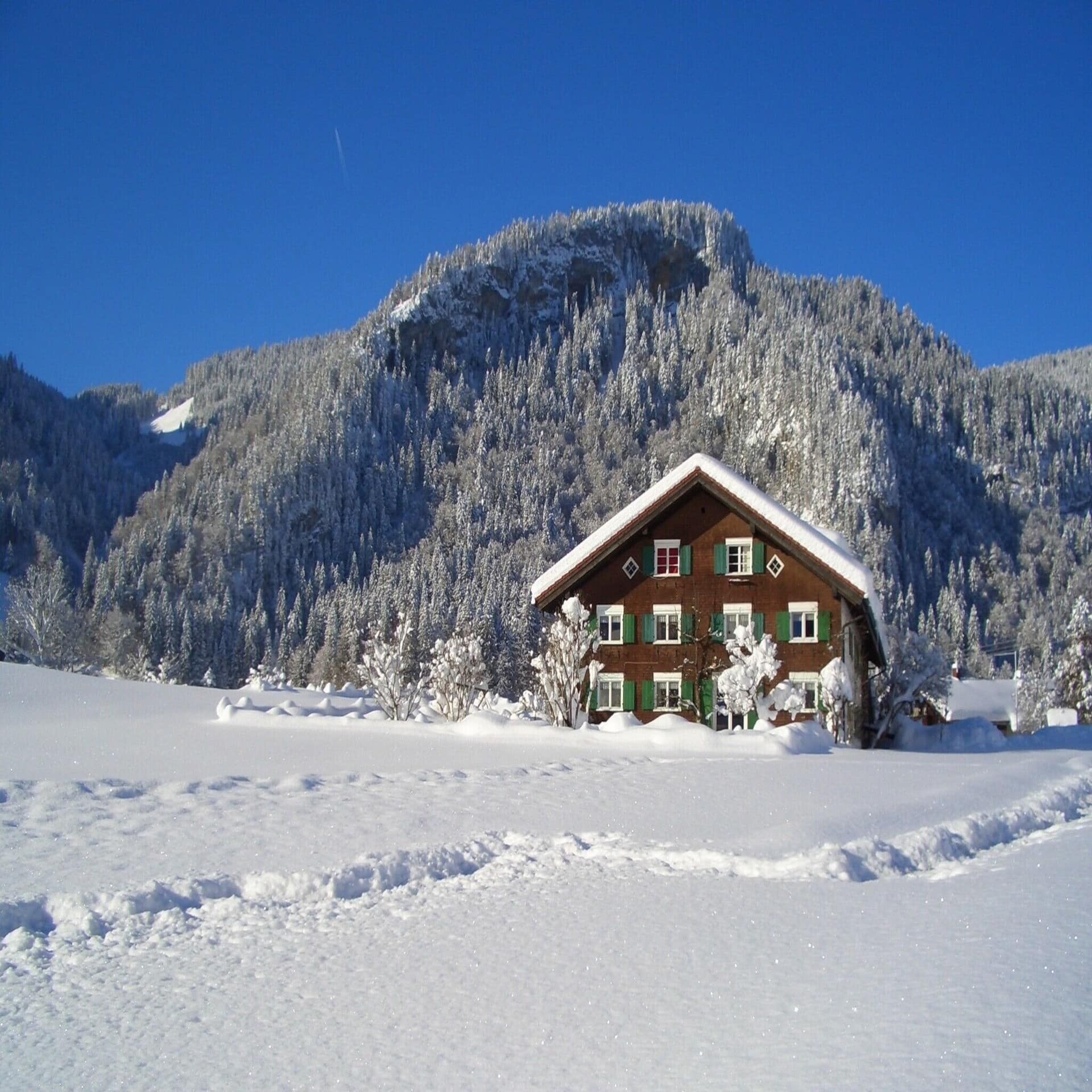 Ein typisch bayerisches Holzhaus in verschneiter Berglandschaft in Oberstdorf. Die Sonne scheint. 