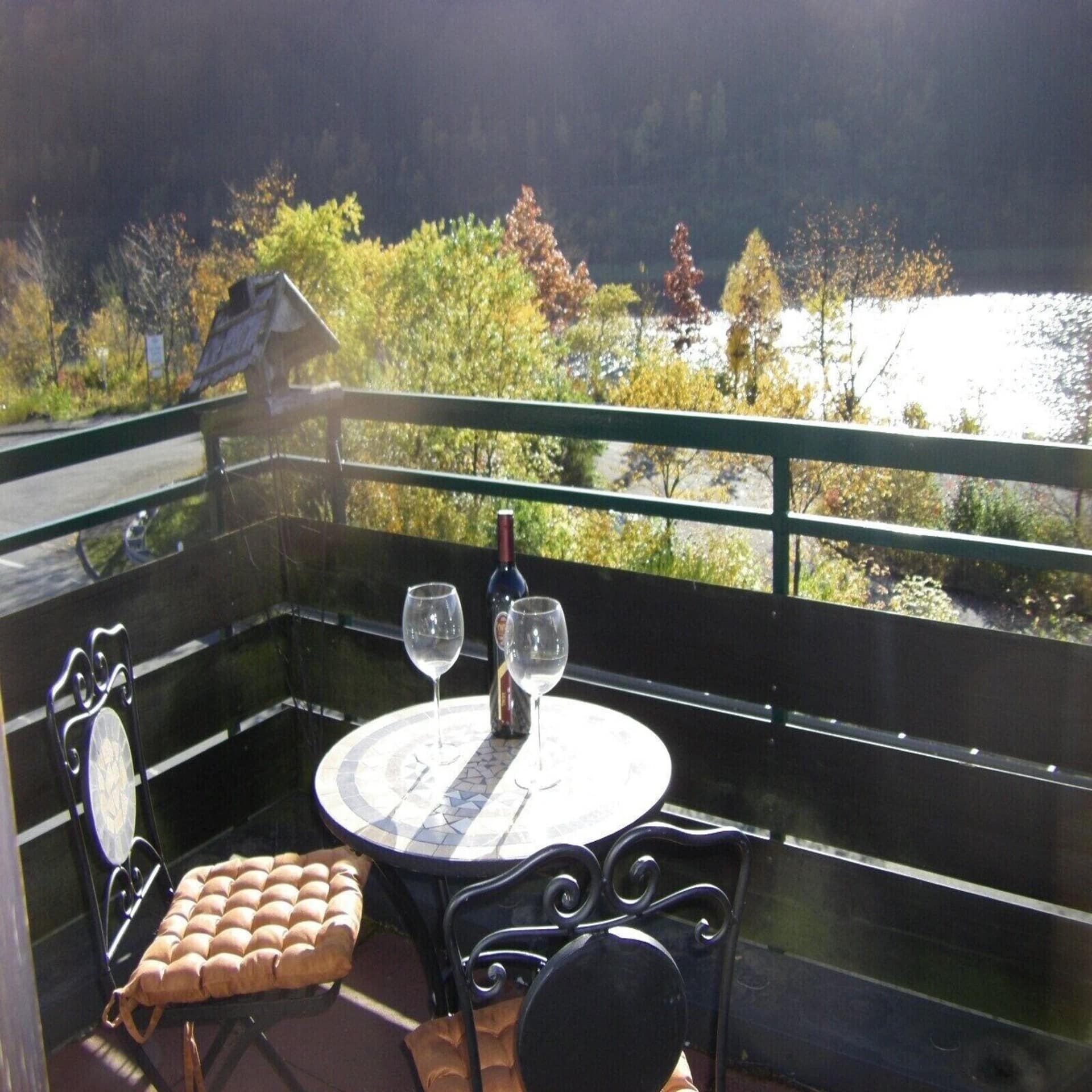 Balkon mit Tisch, 2 Stühlen und Wein sowie Blick auf einen See.