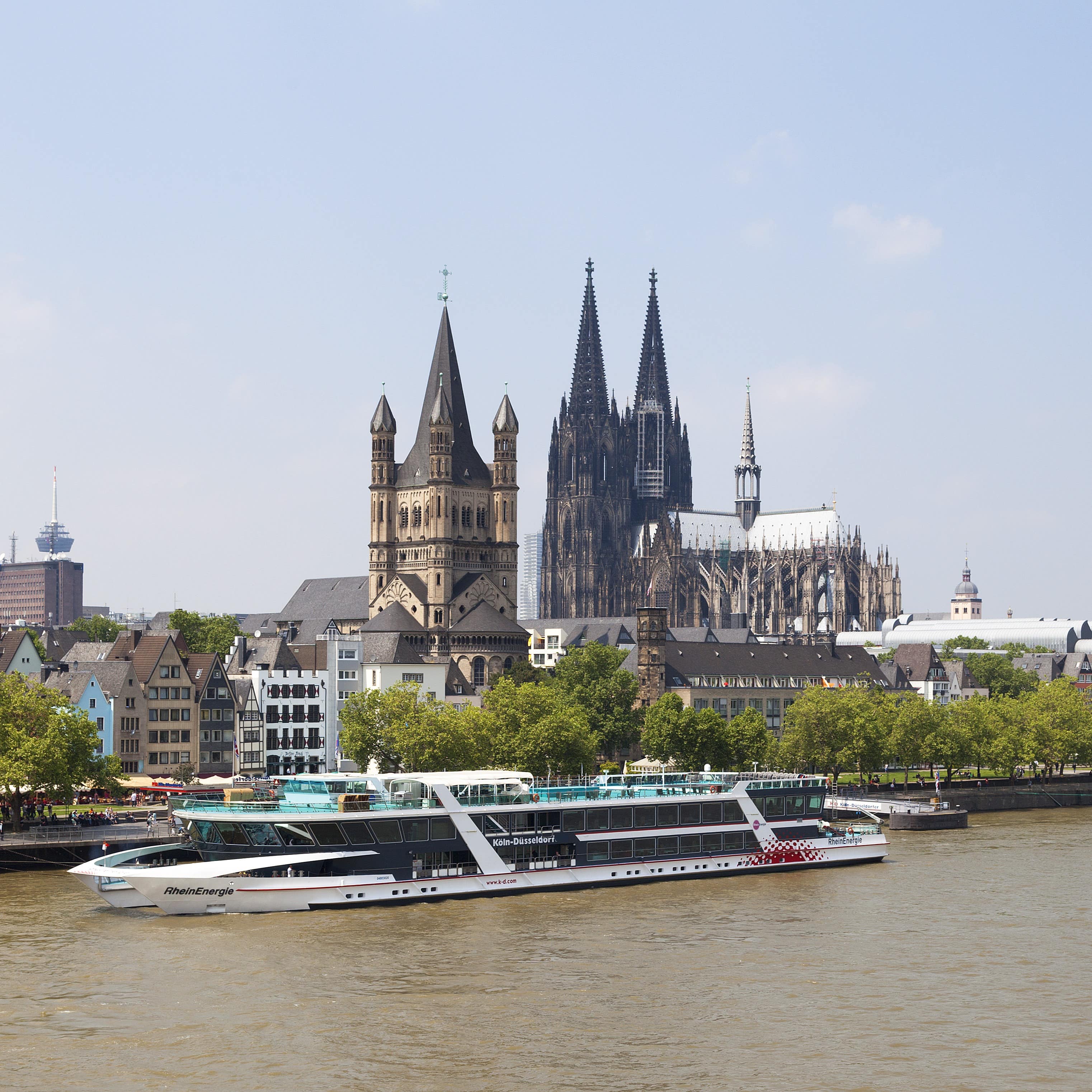 Blick über den Rhein auf ein ankerndes Ausflugsboot, dahinter die Stadt und der Dom.