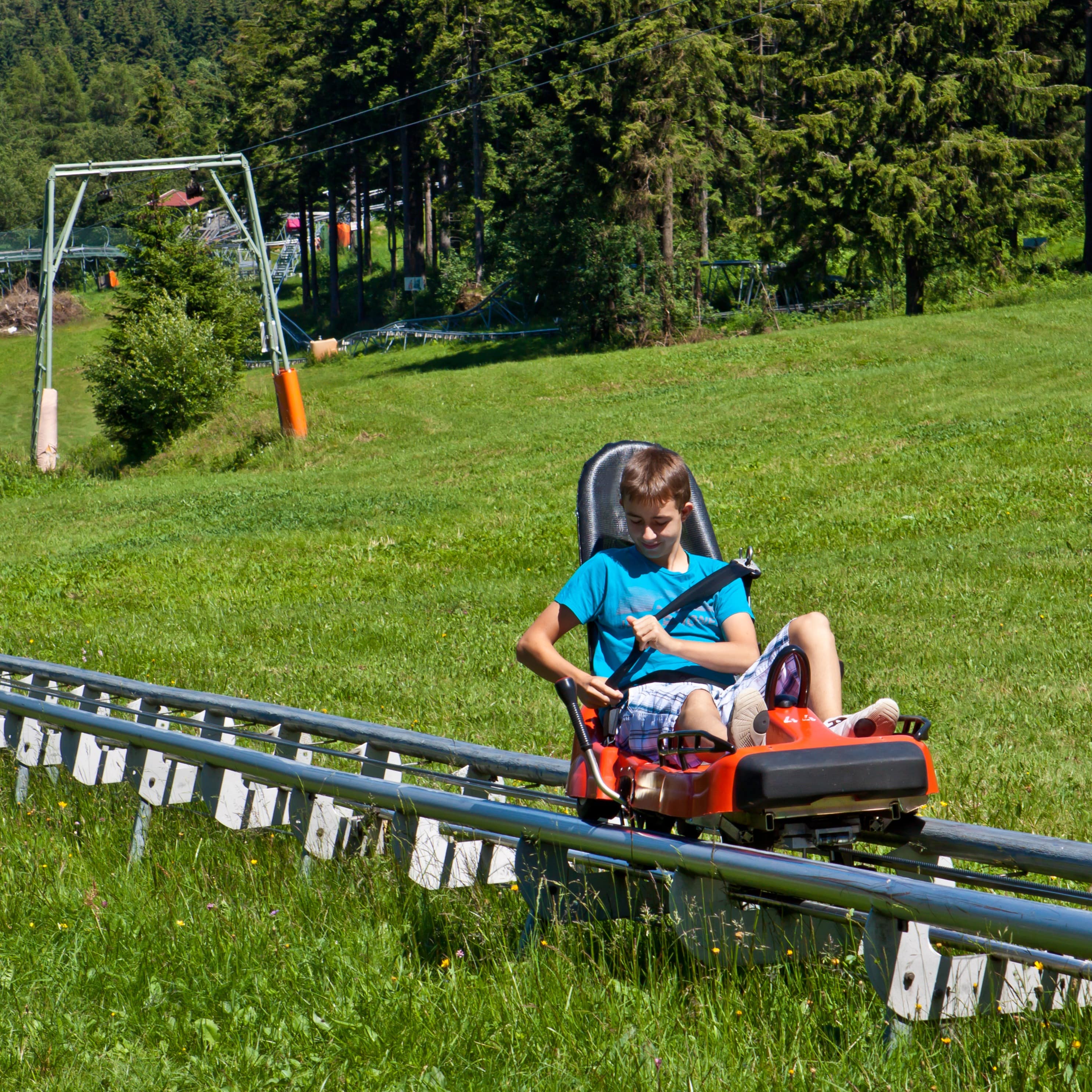 Ein Junge in Sommerkleidung gurtet sich gerade für eine Fahrt mit der Sommerrodelbahn an.