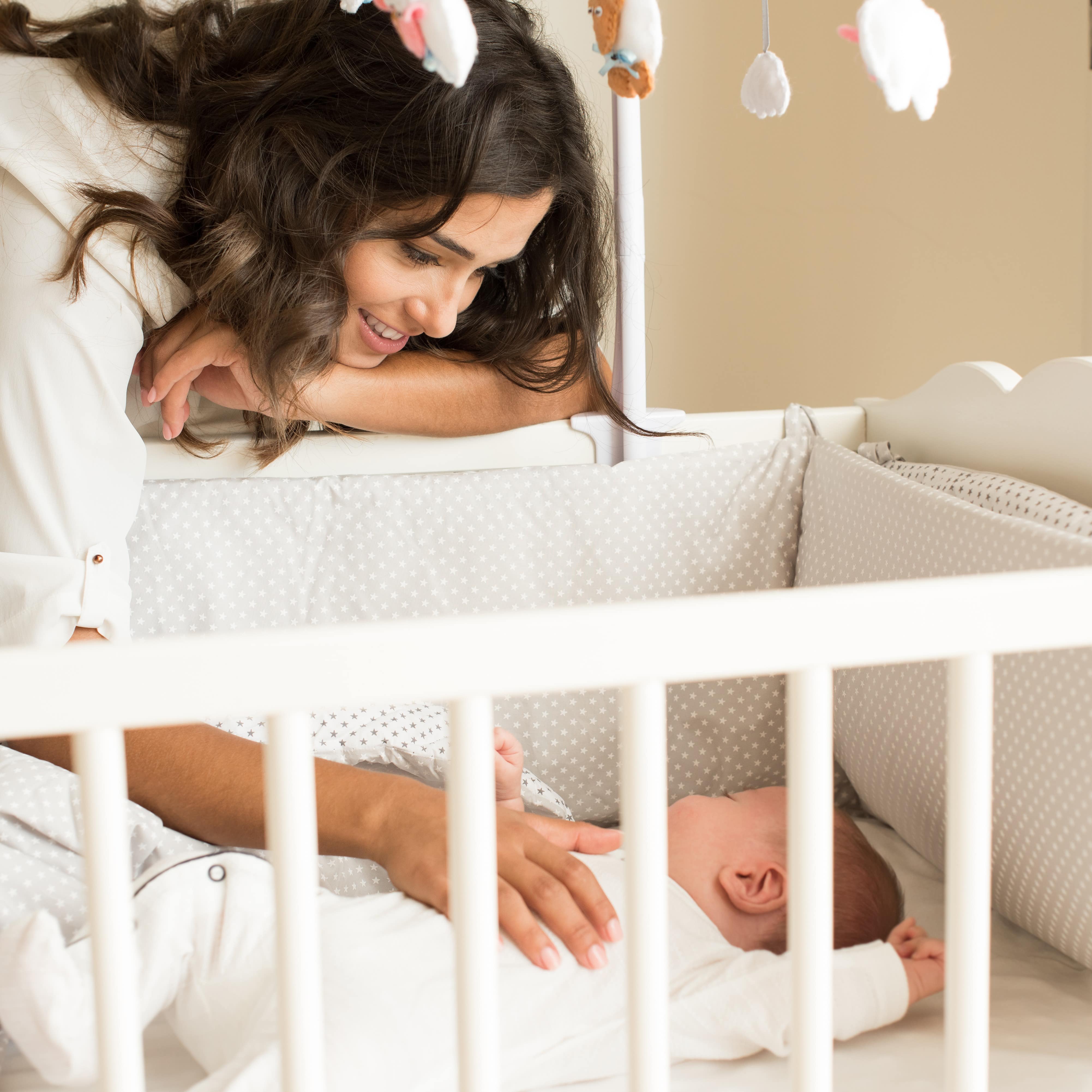 Mutter mit der Hand auf dem Bauch eines Babys, das in einem weißen Babybett liegt.