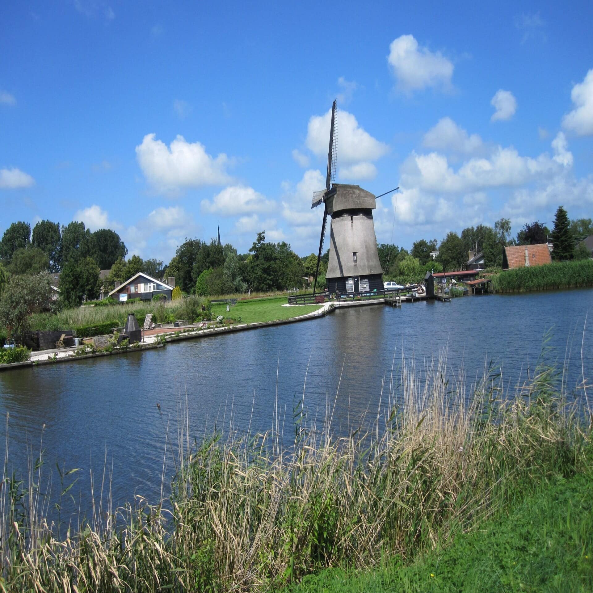 Blick über Wasser auf eine Windmühle und Häuser.