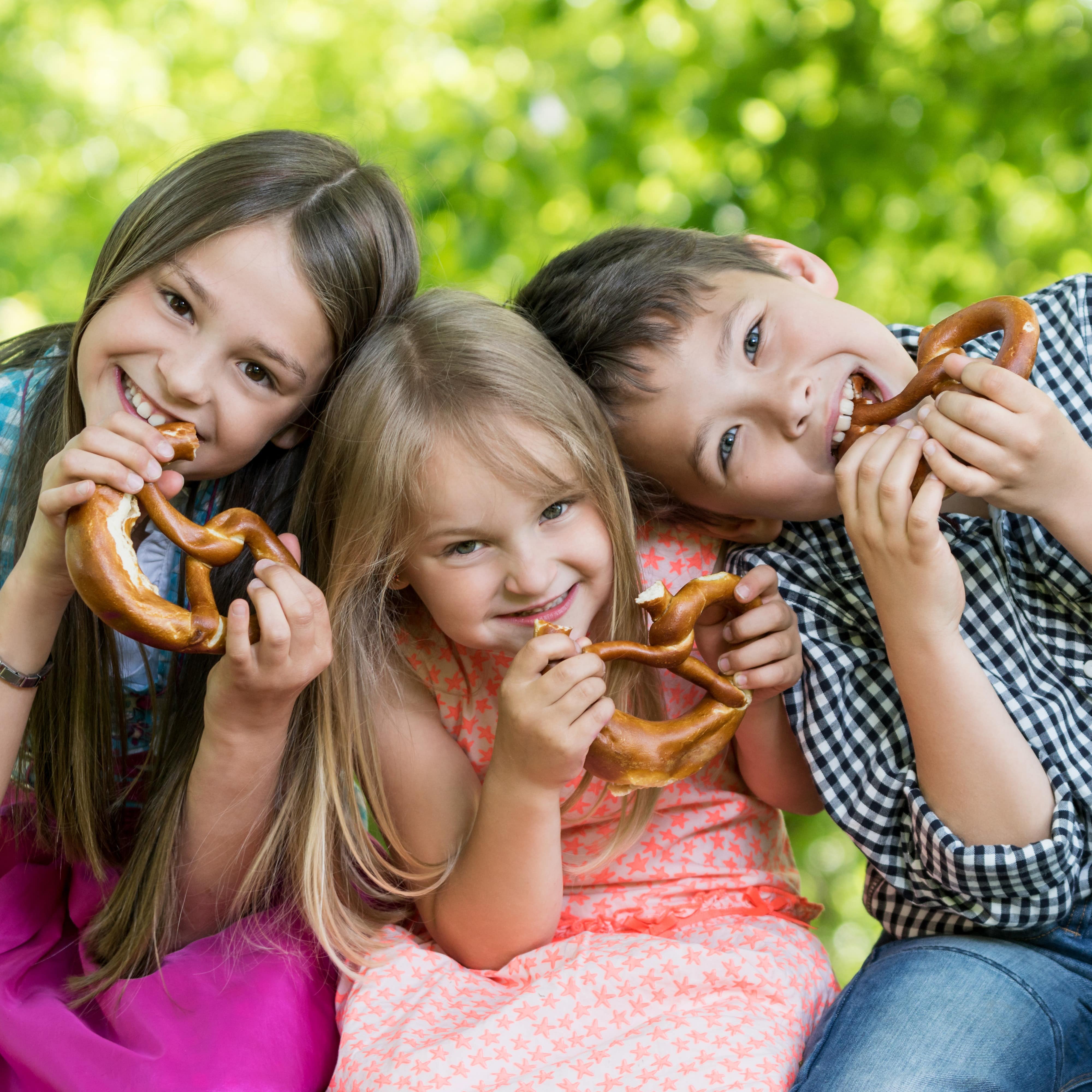 2 Mädchen und 1 Junge sitzen dicht beieinander und essen Brezeln.