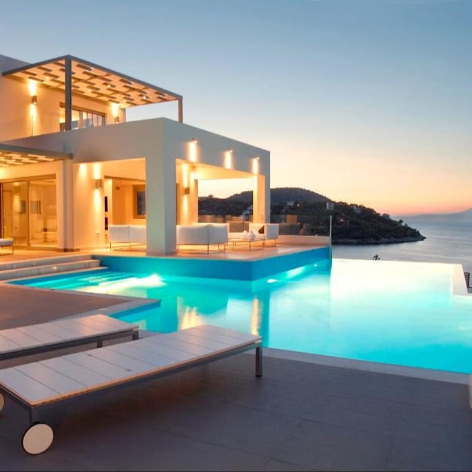 Elegantes weißes Ferienhaus in Griechenland mit großem Infinity-Pool, Liegen und Blick über eine Bucht