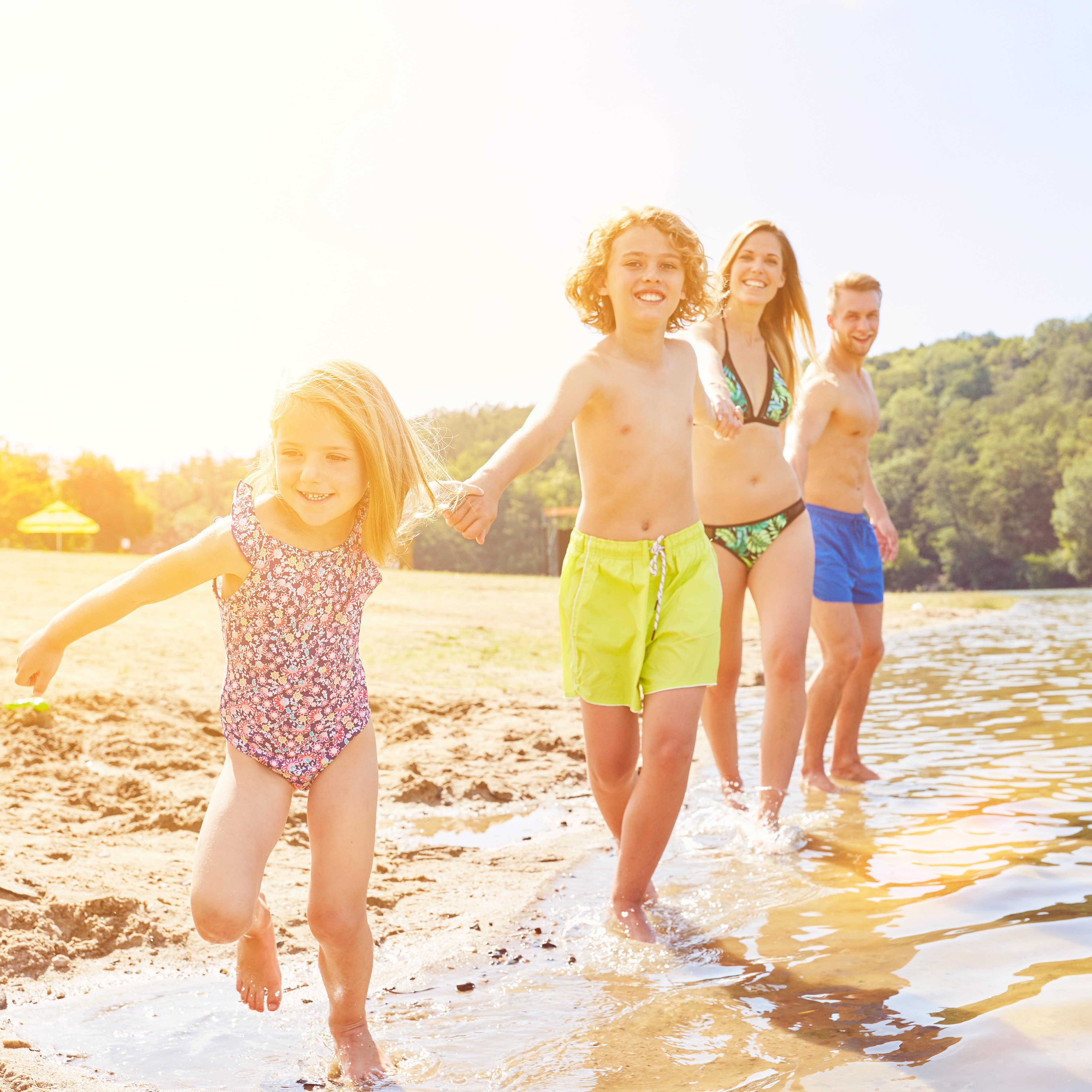 Vierköpfige Familie hält sich an den Händen und steht im flachen Wasser eines Waldsees.