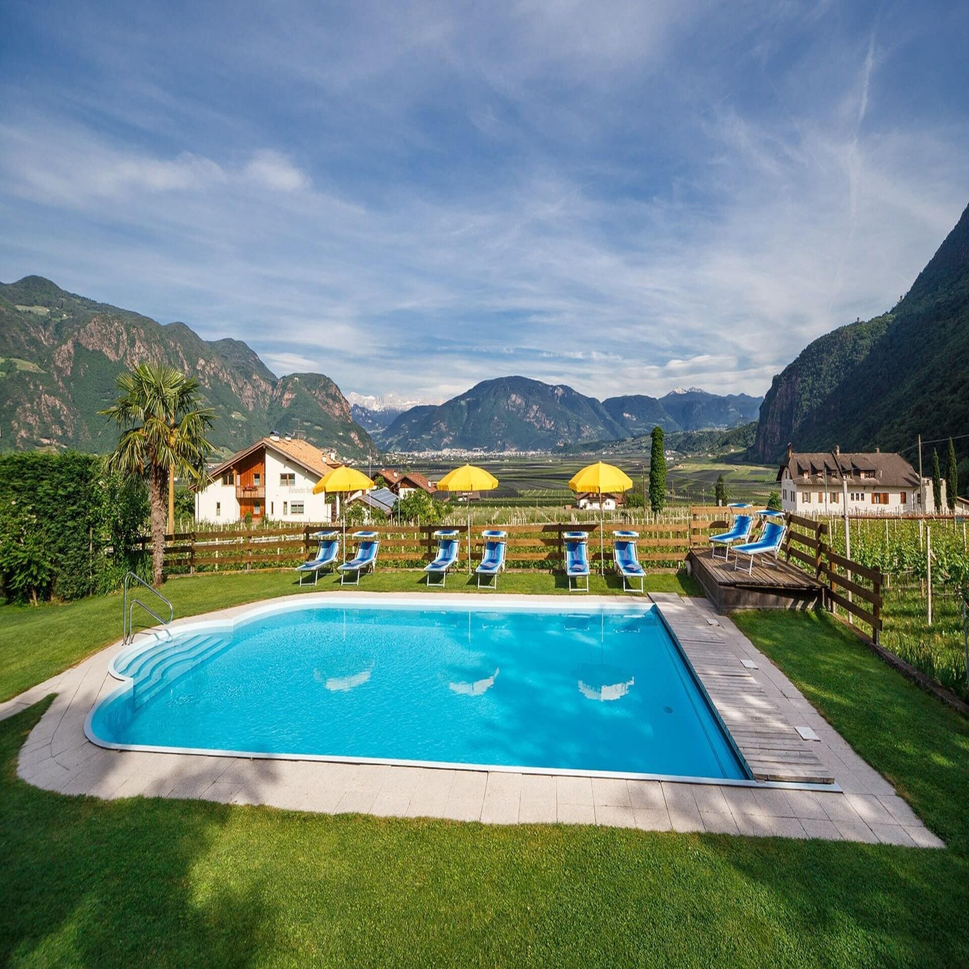 Garten mit Pool, Liegestühlen und Sonnenschirmen und Blick auf Weinberge und Berge. 