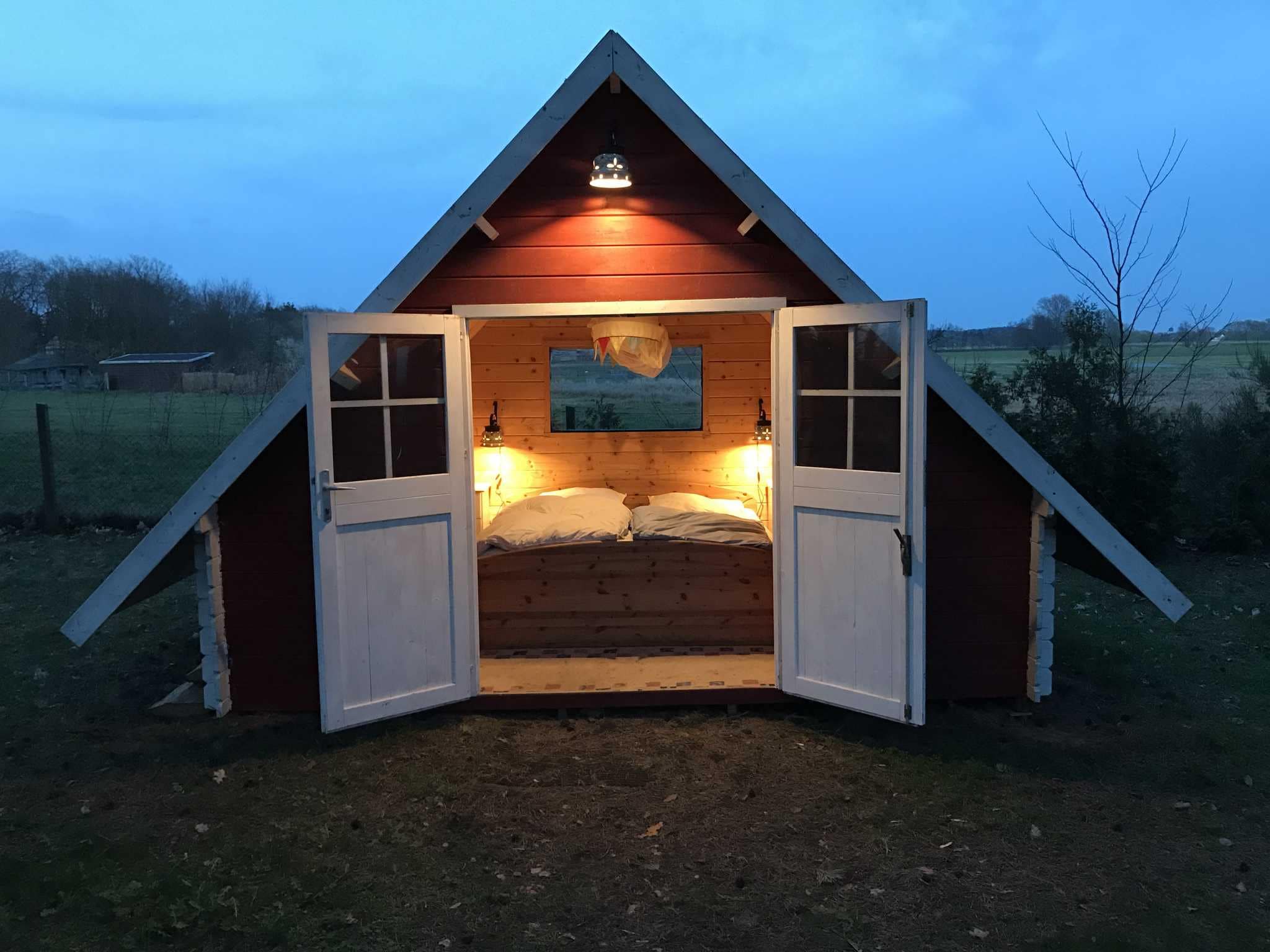 Kleine Finnhütte mit einer geöffneten Flügeltür und Blick auf ein Bett