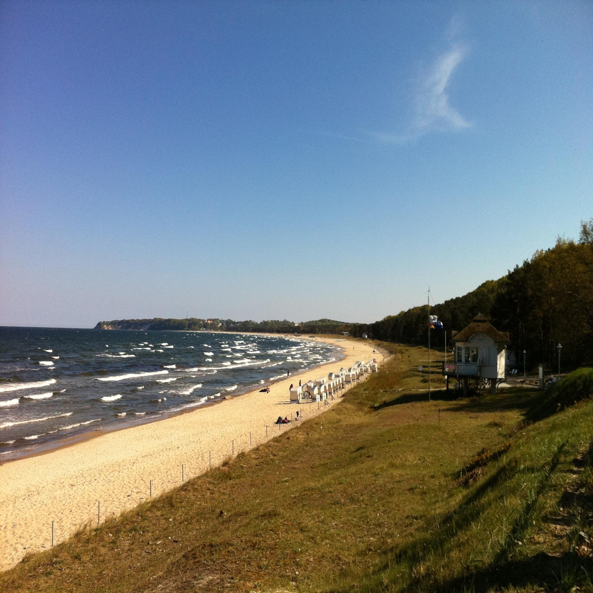 Blick vom Garten auf den Strand mit Strandkörben und das Meer.