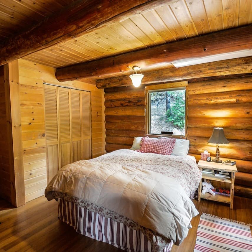 Dieses Schlafzimmer einer Holzhütte ist komplett in Holz gehalten, vor dem Fenster steht ein kuscheliges Bett.