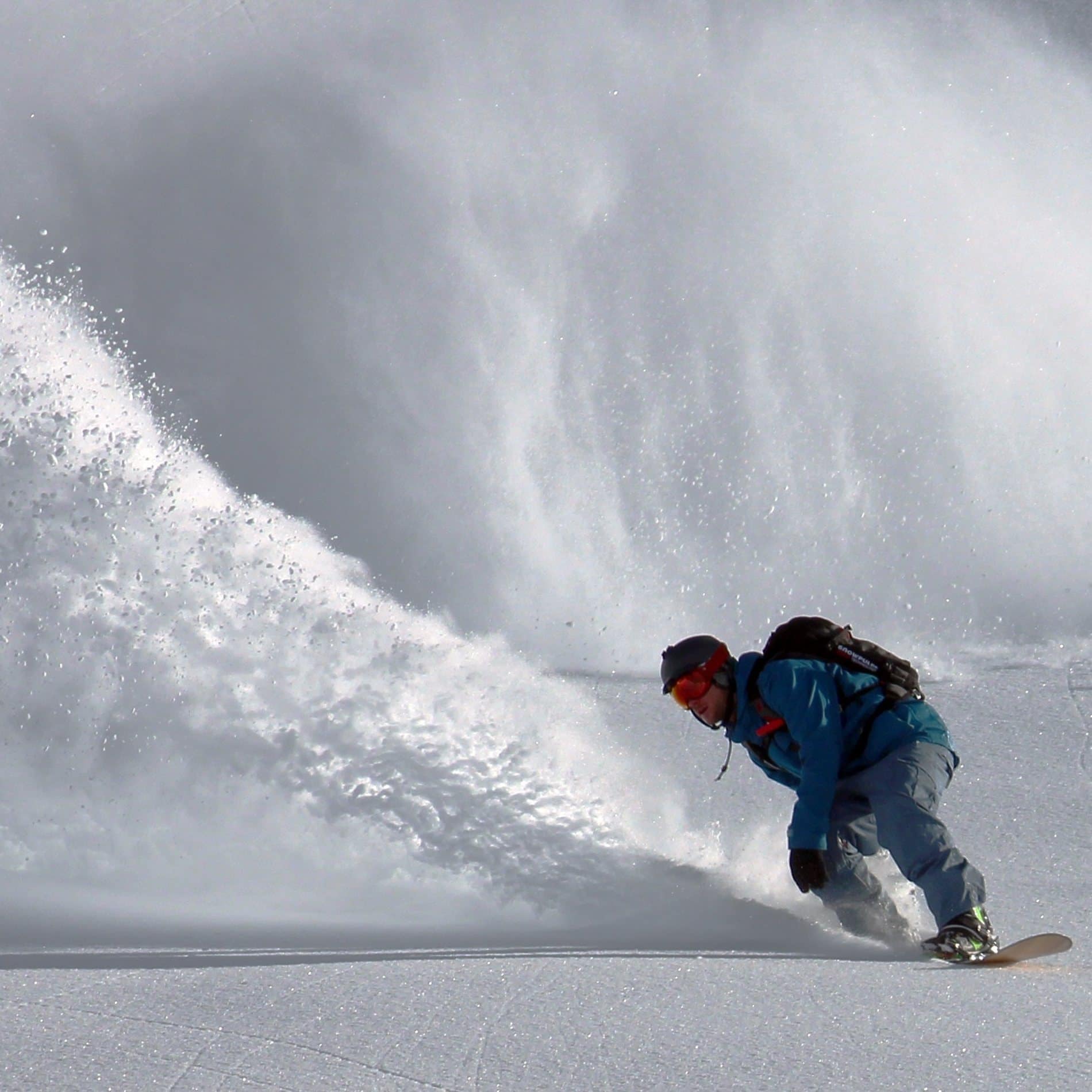 Ein Snowboarder mit Skibrille lässt den Schnee hoch aufstieben in einem Skigebiet in Tirol