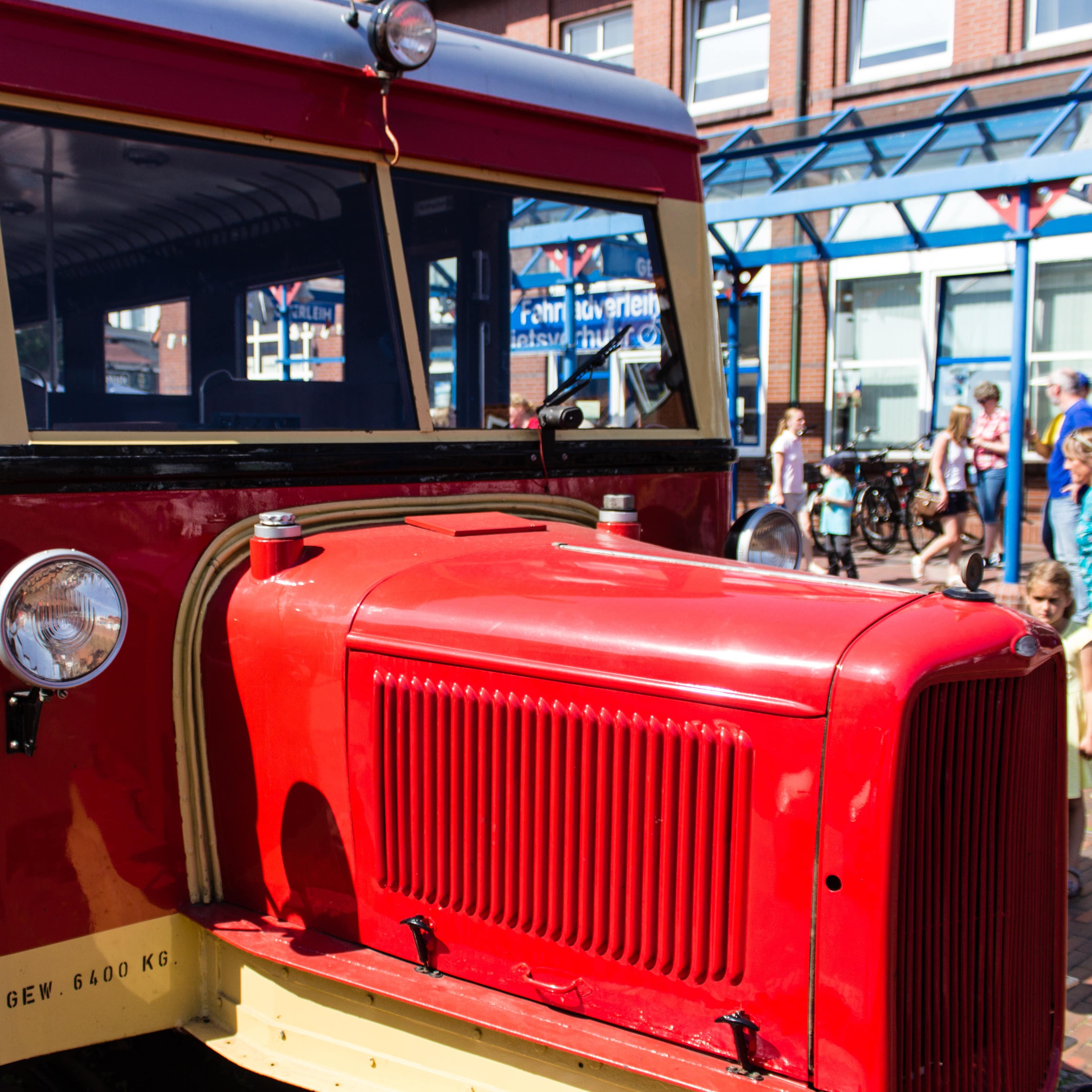 Die rote-gelbe Inselbahn von Borkum, dahinter ein Mädchen und Urlauber.