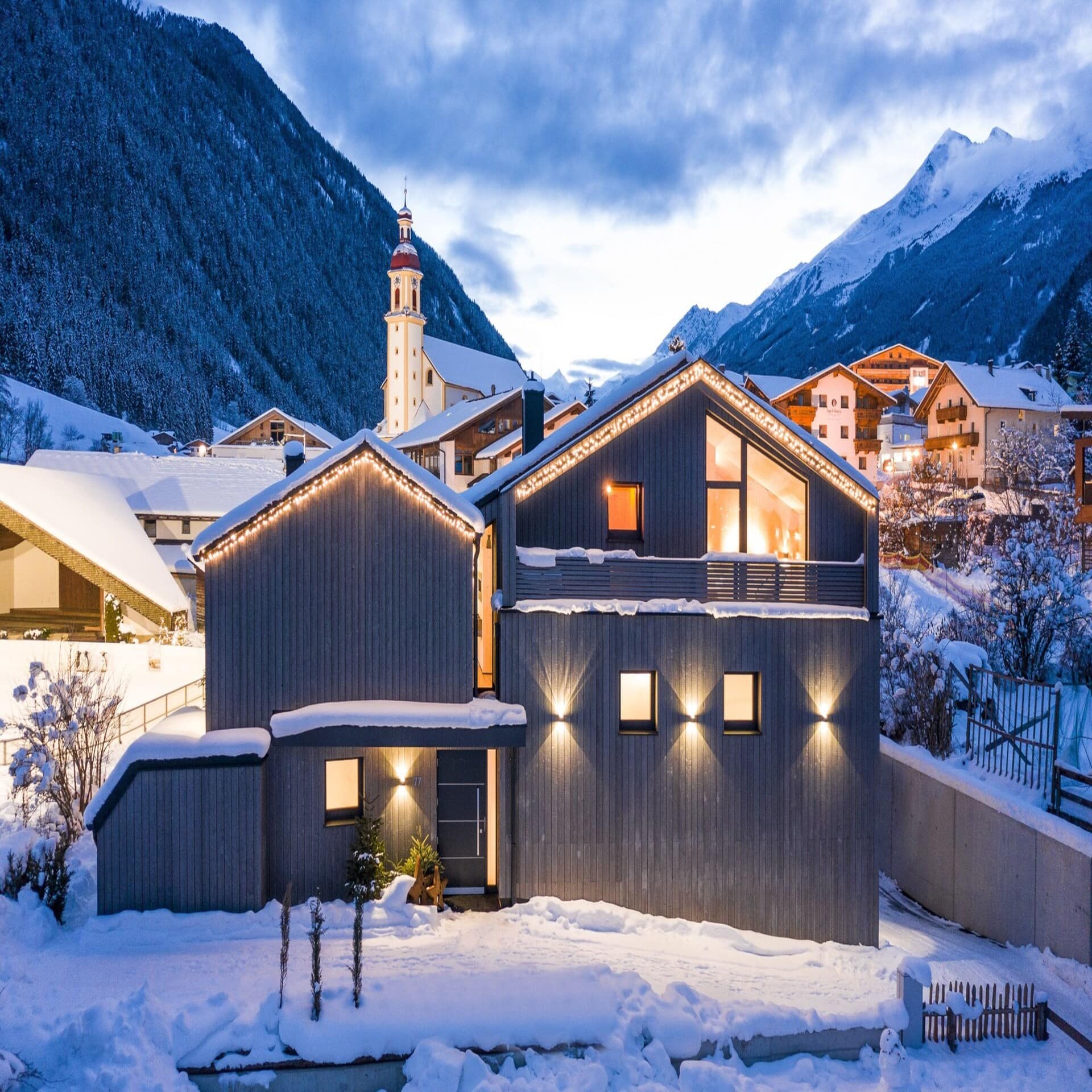 Modernes, erleuchtetes Holzhaus in einem verschneiten Ort in der Abenddämmerung.