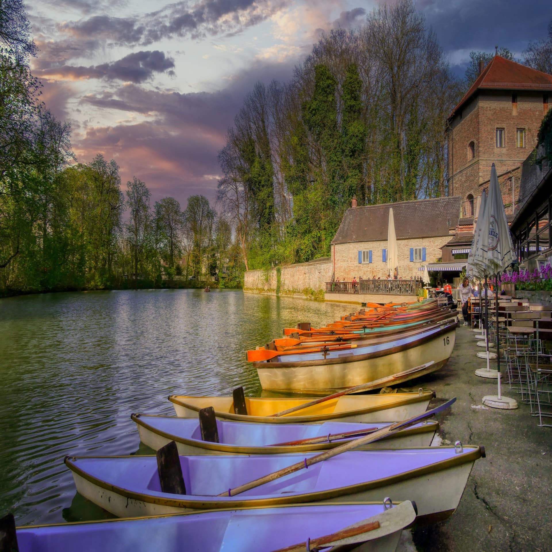 Bunte Ruderboote am Ufer vor historischer Kulisse.