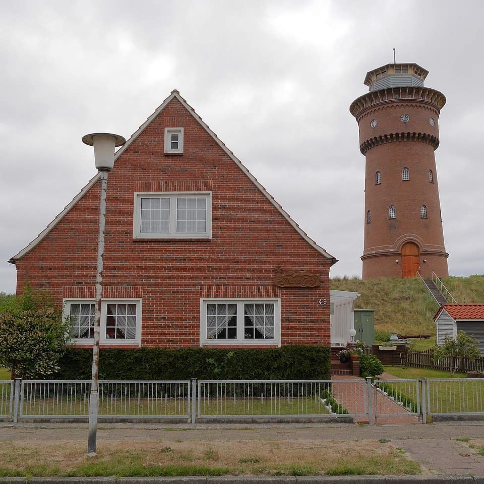 Typisches Friesenhaus mit dem historischen Insel-Leuchtturm im Hintergrund.