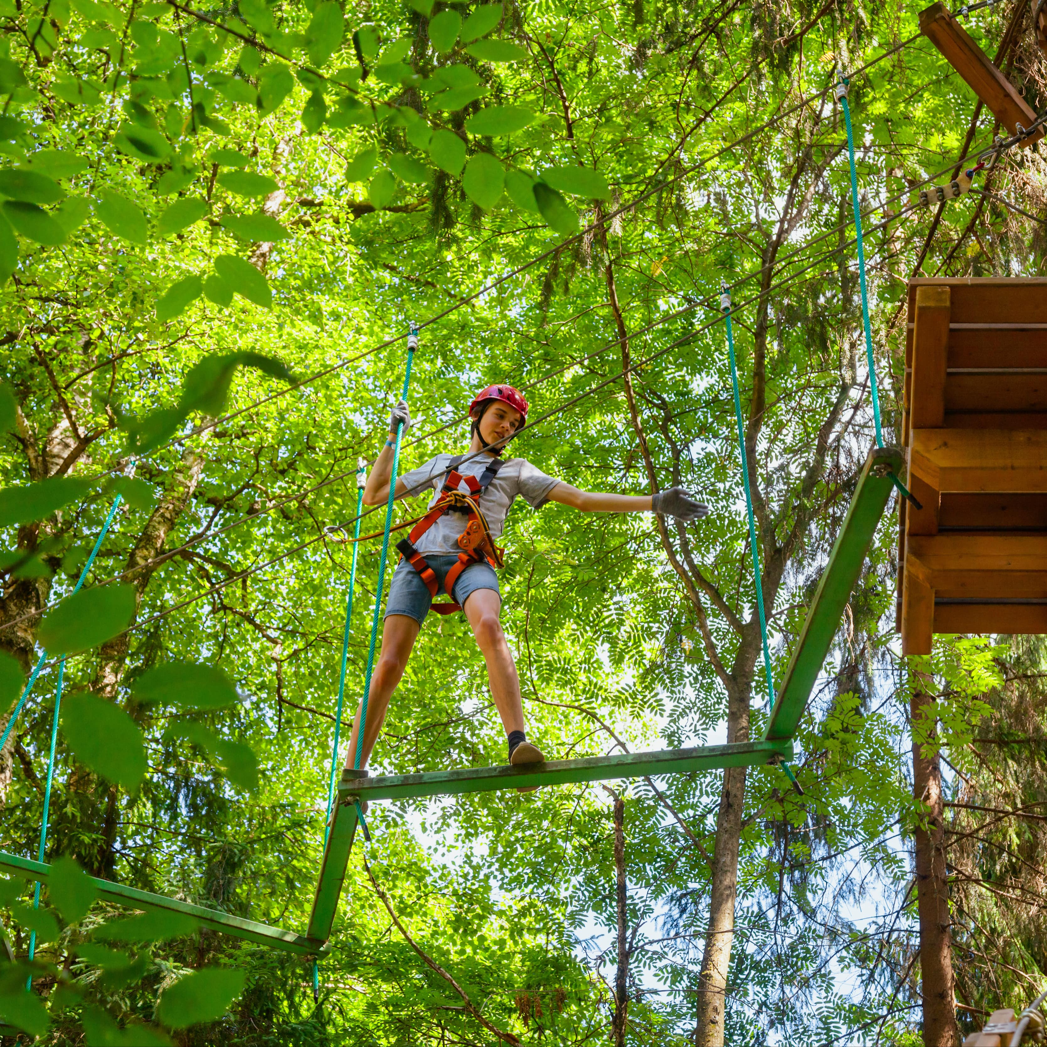 Junge im Teenageralter balanciert auf einem Holz in einem Kletterpark. 