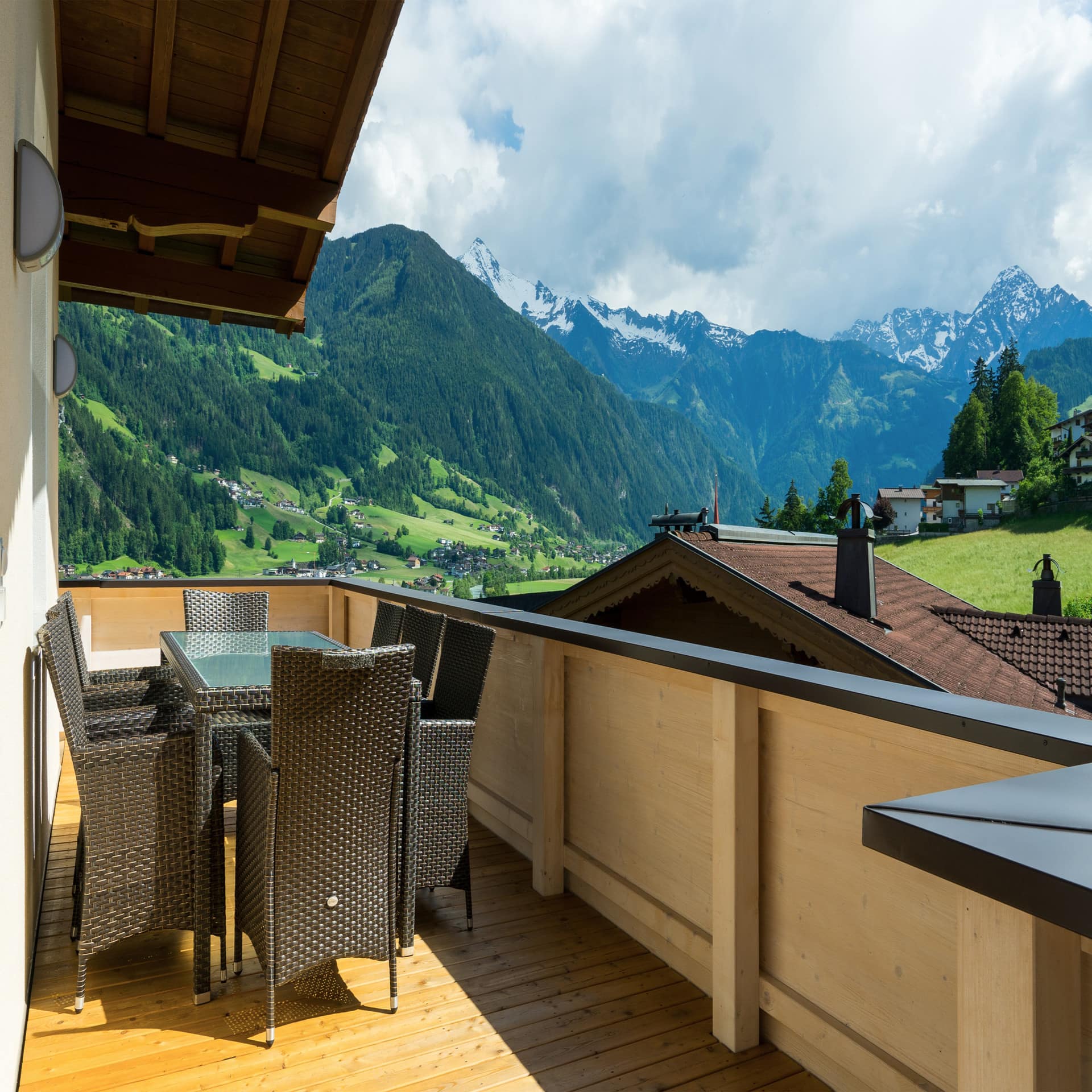 Blick von einem Balkon mit Tisch und 8 Stühlen auf das sonnige Zillertal im Sommer. 