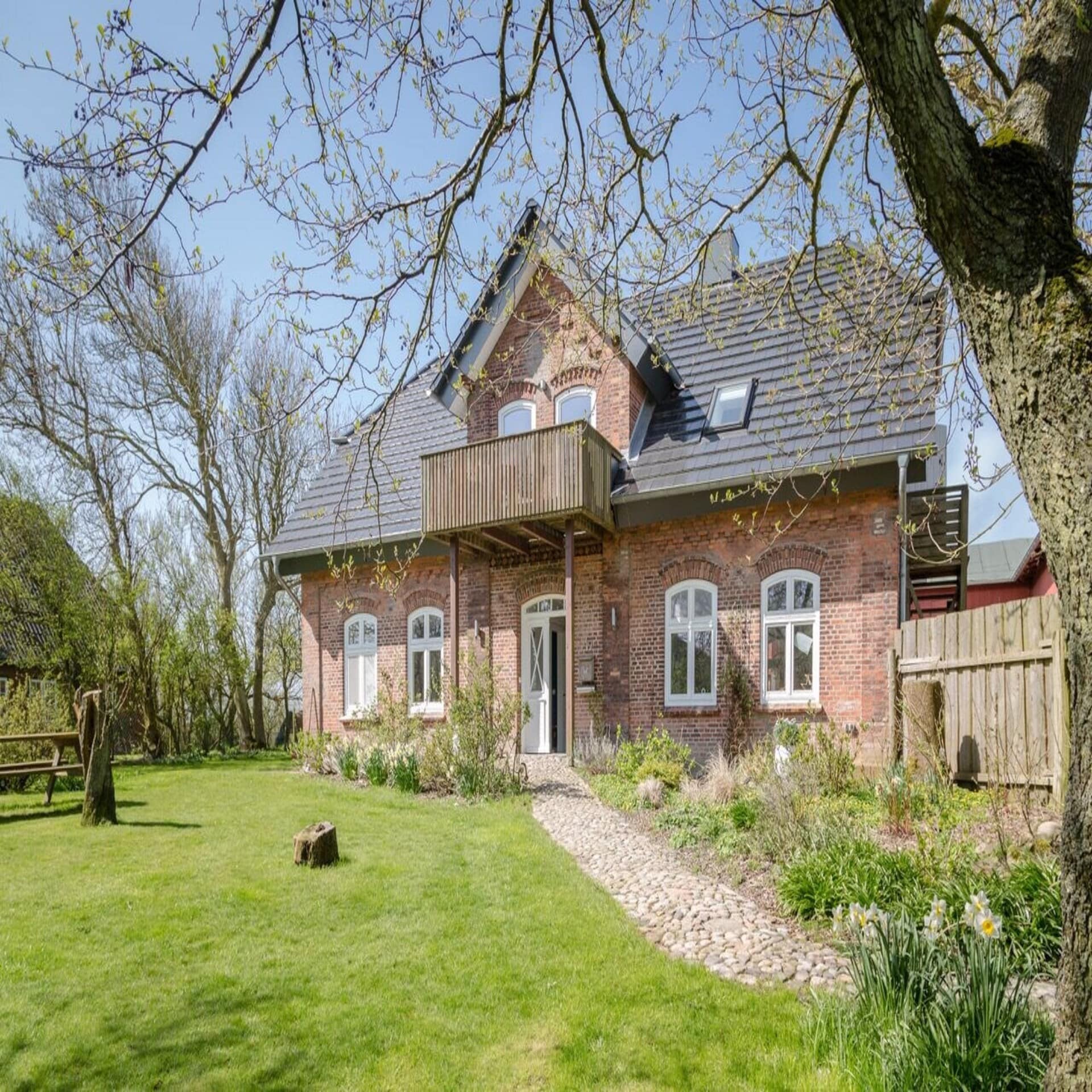 Restauriertes Bauernhaus aus rotem Backstein in einem großen, grünen Garten.