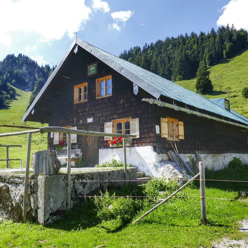 Eine Hütte an einem Hang umgeben von Wiesen und Wäldern