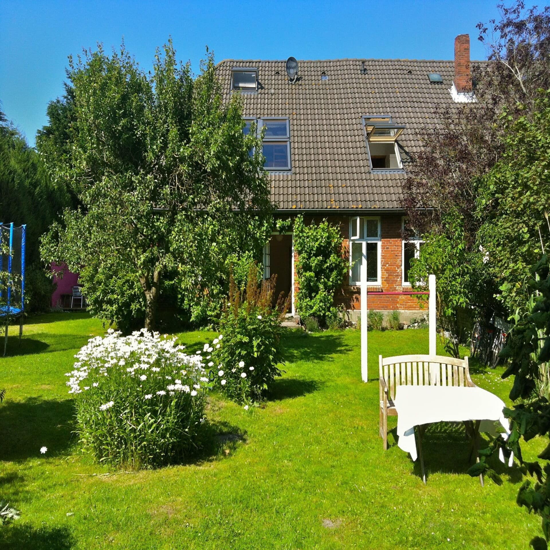 Rotes Bauernhaus mit blühendem Garten und einer Sitzbank mit Tisch darin.