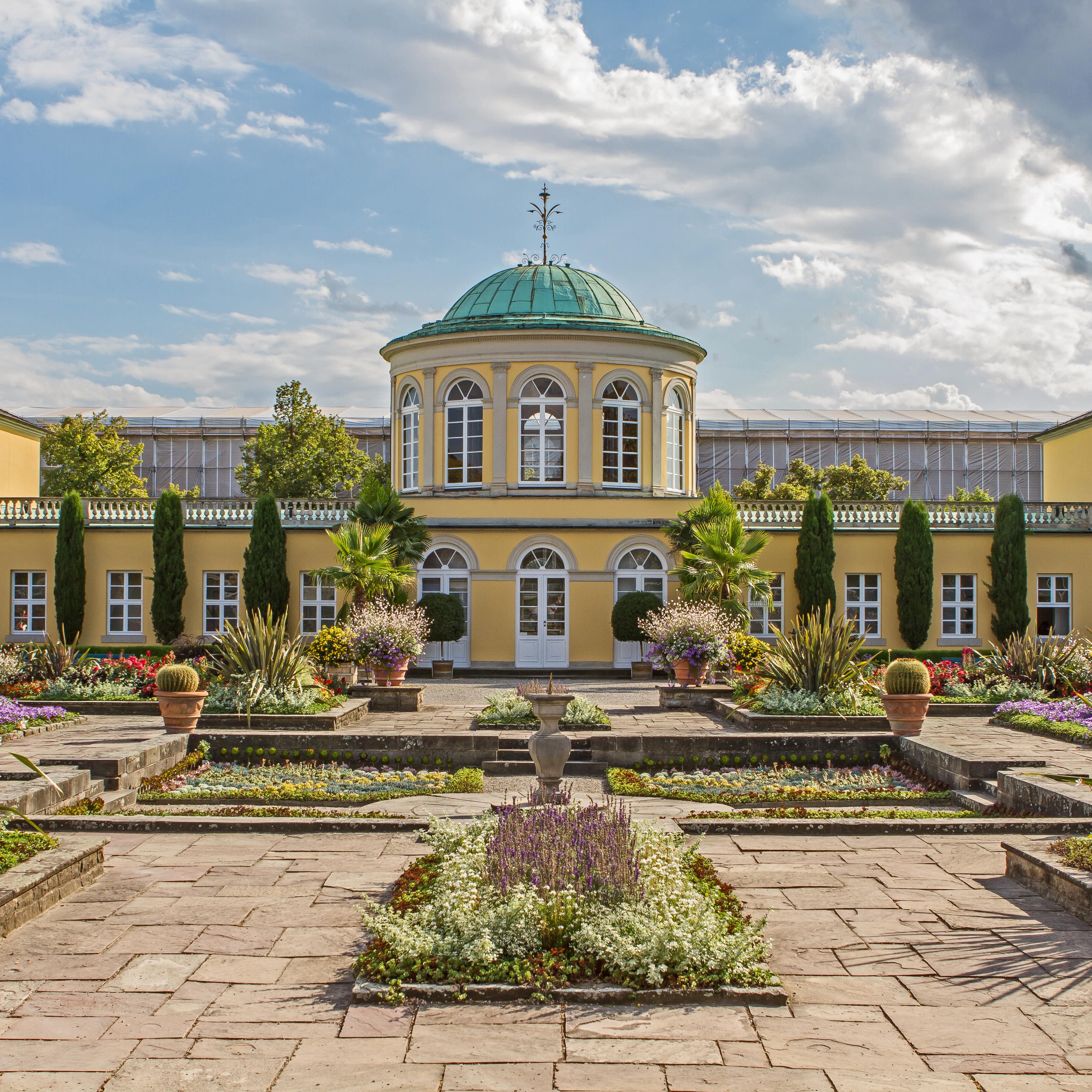 Gelbes Barockgebäude, davor ein Garten mit Blumen in den Herrenhäuser Gärten.