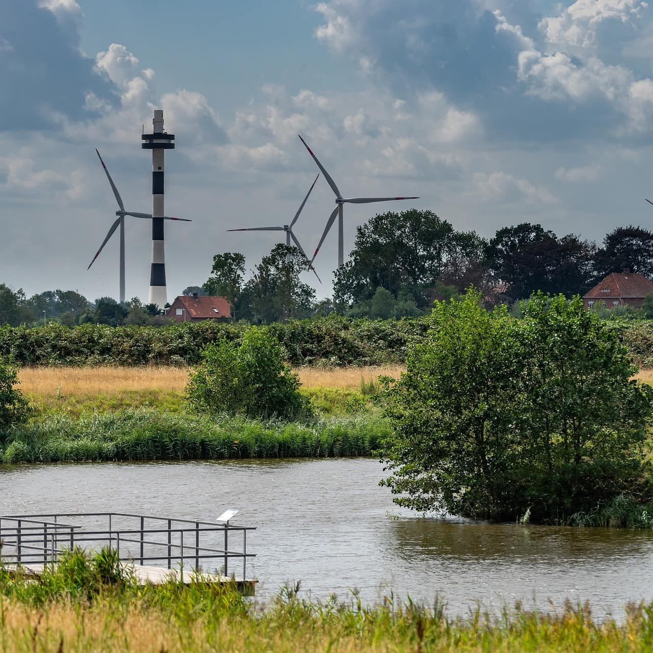 Blick über Wasser und Wiesen hinweg auf Windräder und Häuser in Cuxhaven