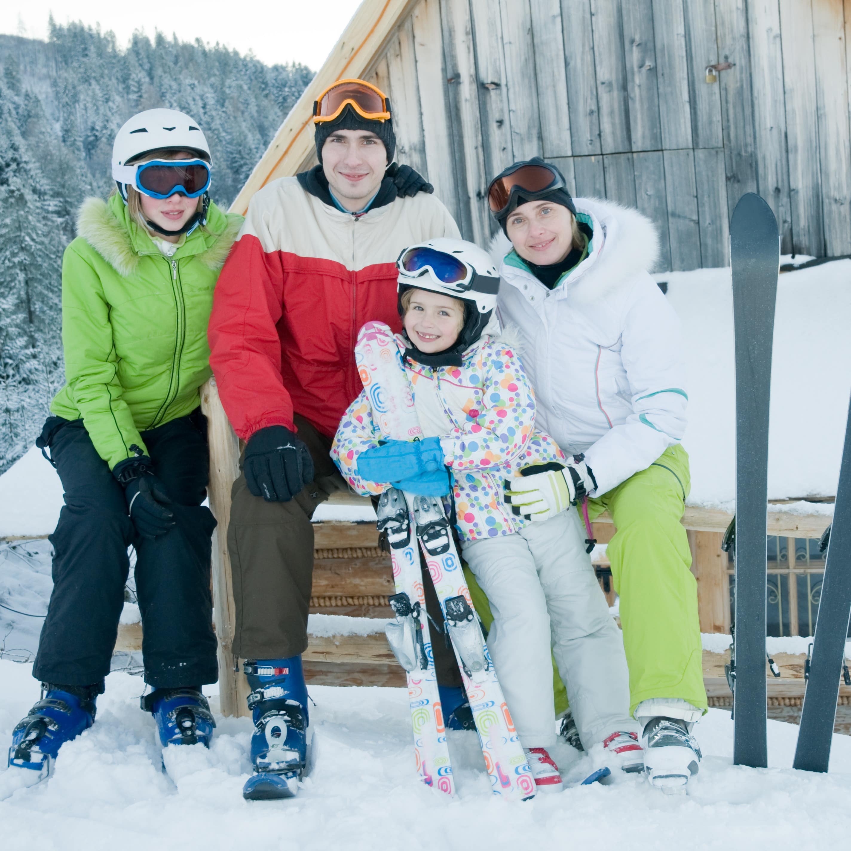 Familie mit zwei Kindern und Skiausrüstung vor einer verschneiten Holzhütte