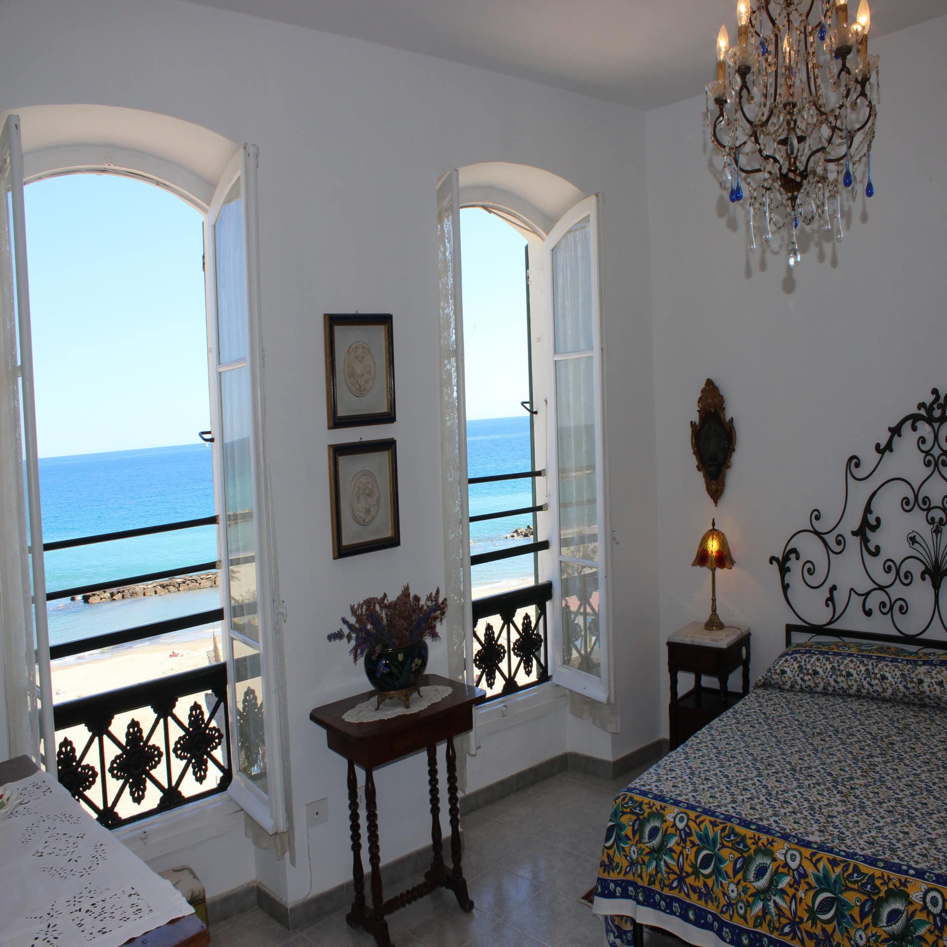 Helles Schlafzimmer mit offenen Fenstern und Blick auf den Strand und das Meer. 