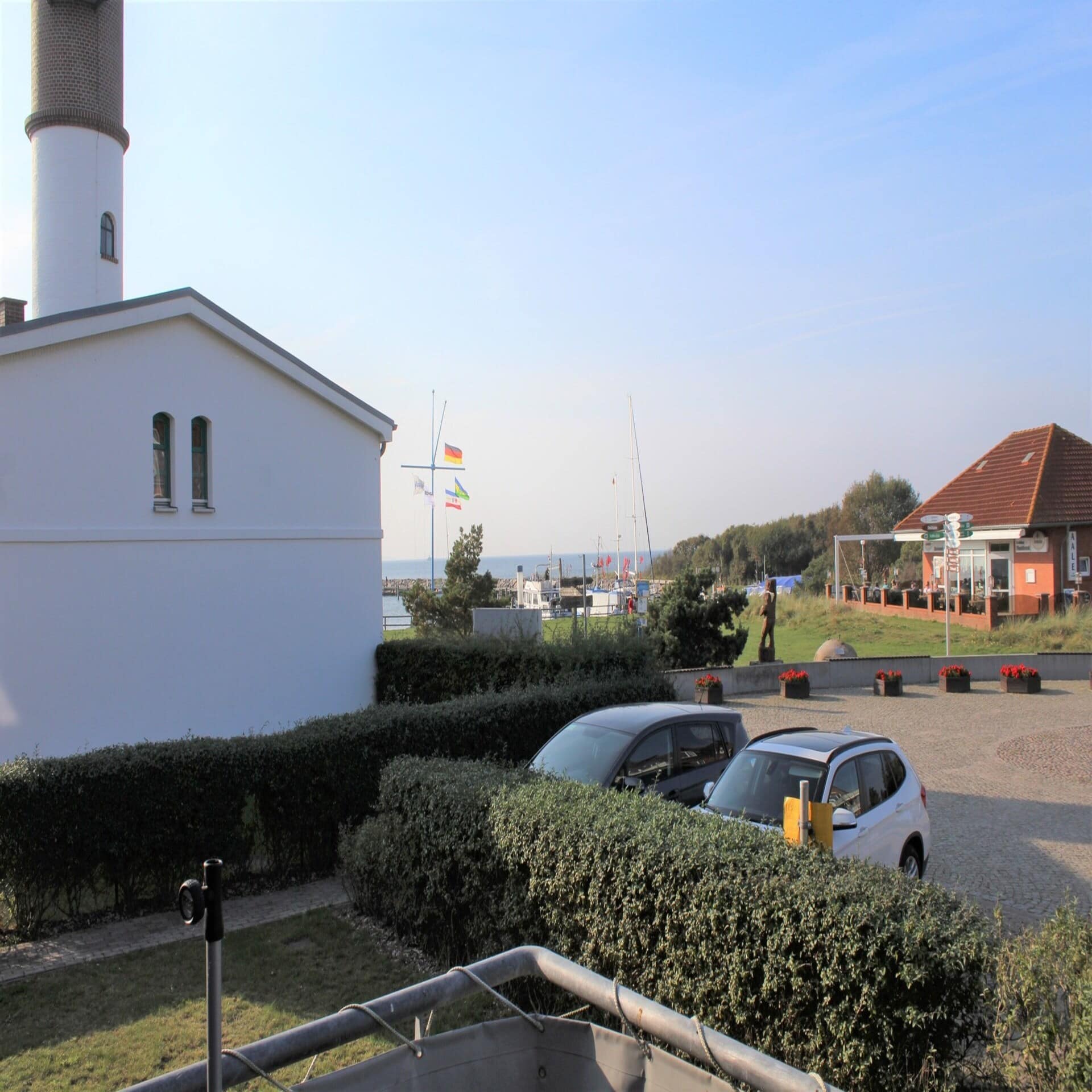 Blick vom Balkon auf einen Parkplatz, den Leuchtturm und das Meer. 