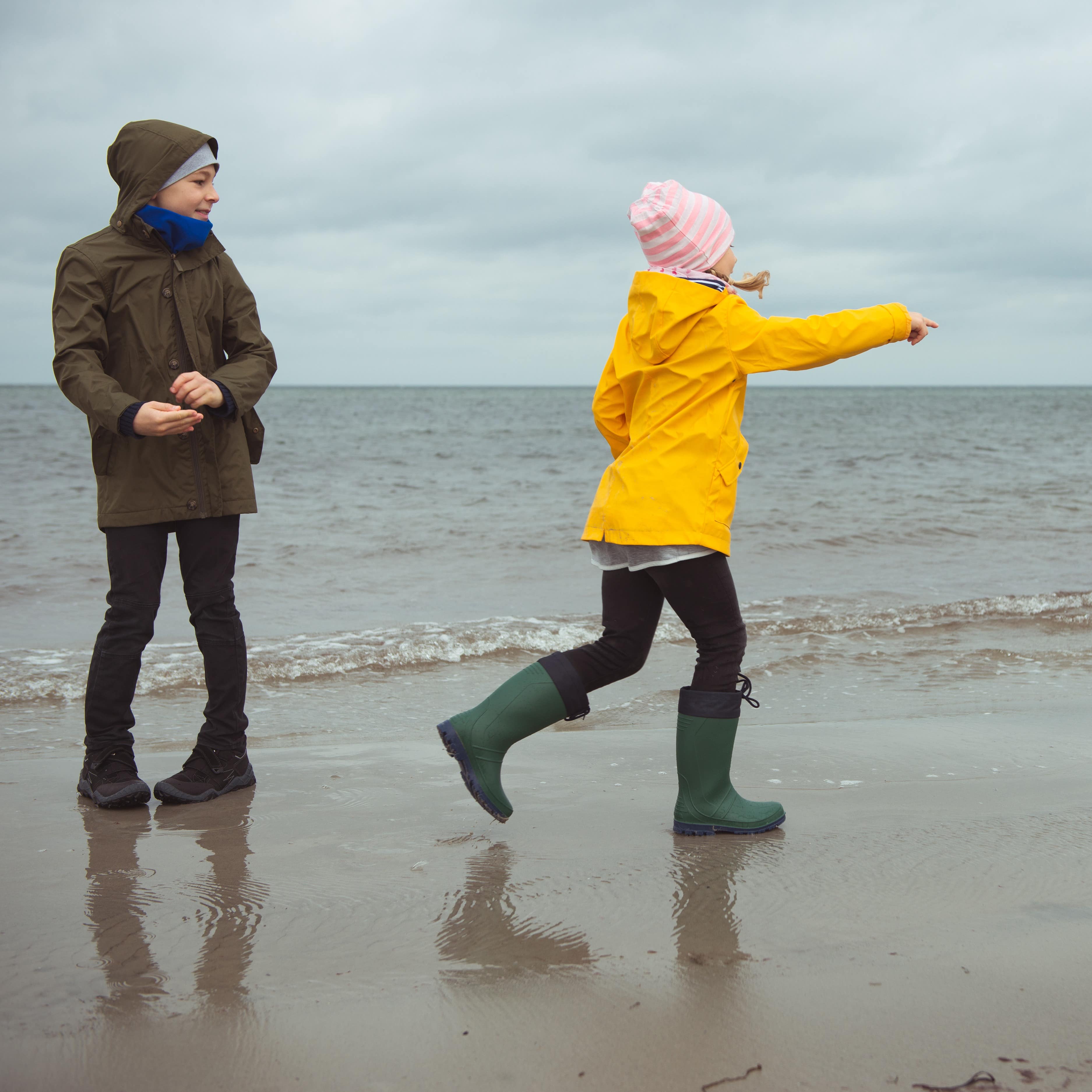 Regenwetter am Strand: 2 ältere Kinder in Regenjacken und Gummistiefeln am Strand. 
