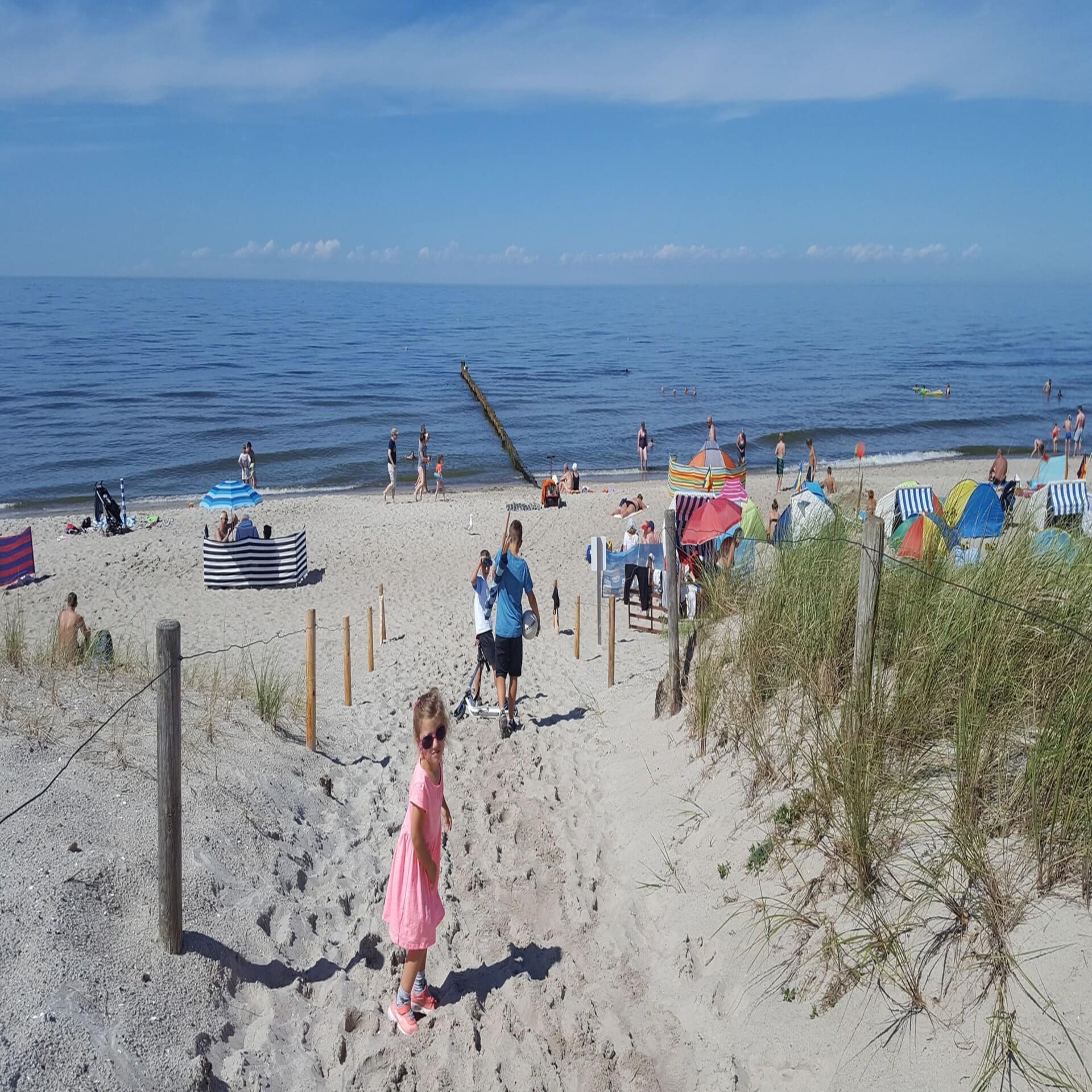 Kinder auf dem Weg zum Strand. Ein Mädchen mit rosa Klein und Sonnenbrille blickt in die Kamera.