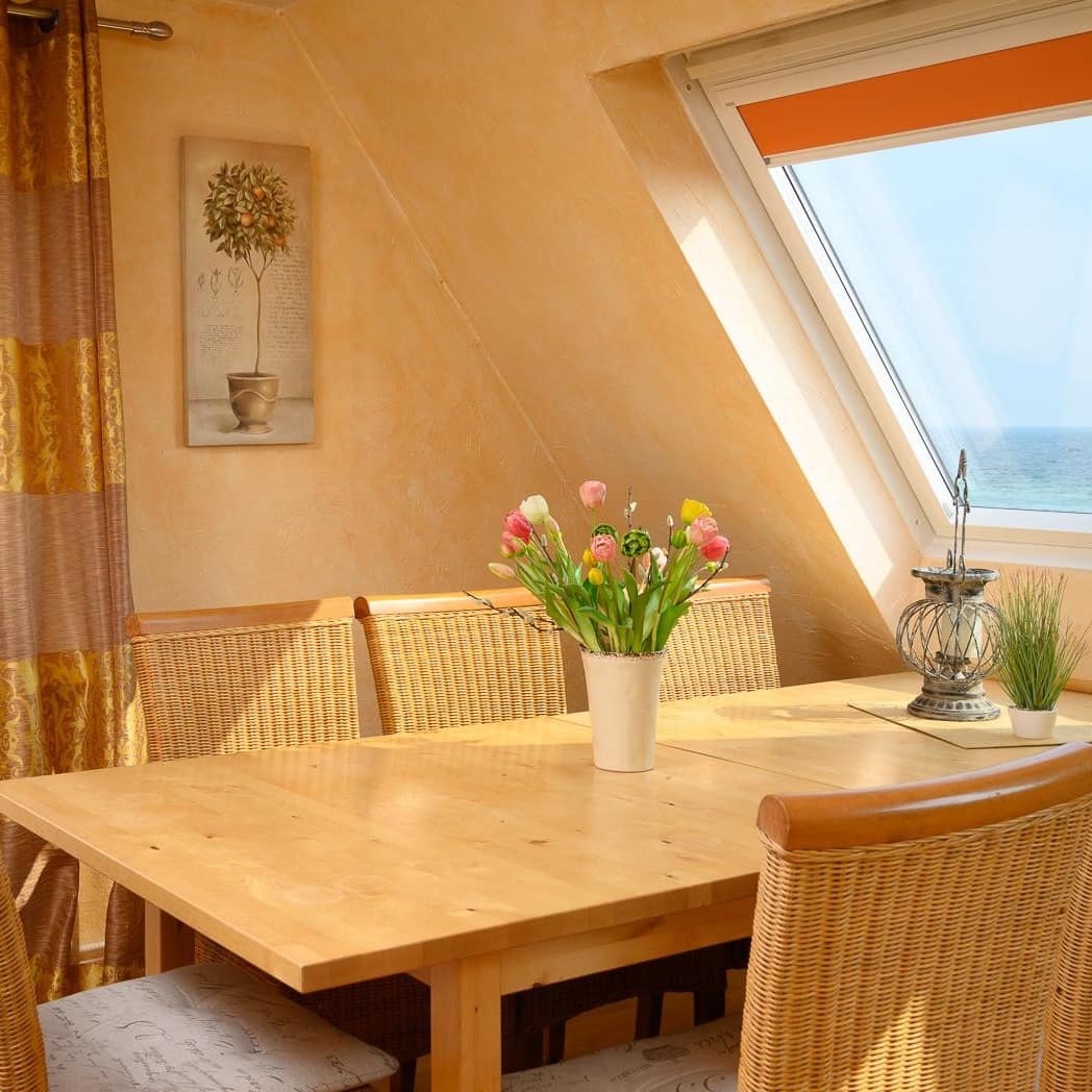 Essbereich in einer Ferienwohnung in der Lübecker Bucht mit Blick auf das Meer, ein Strauß Blumen steht auf dem Tisch
