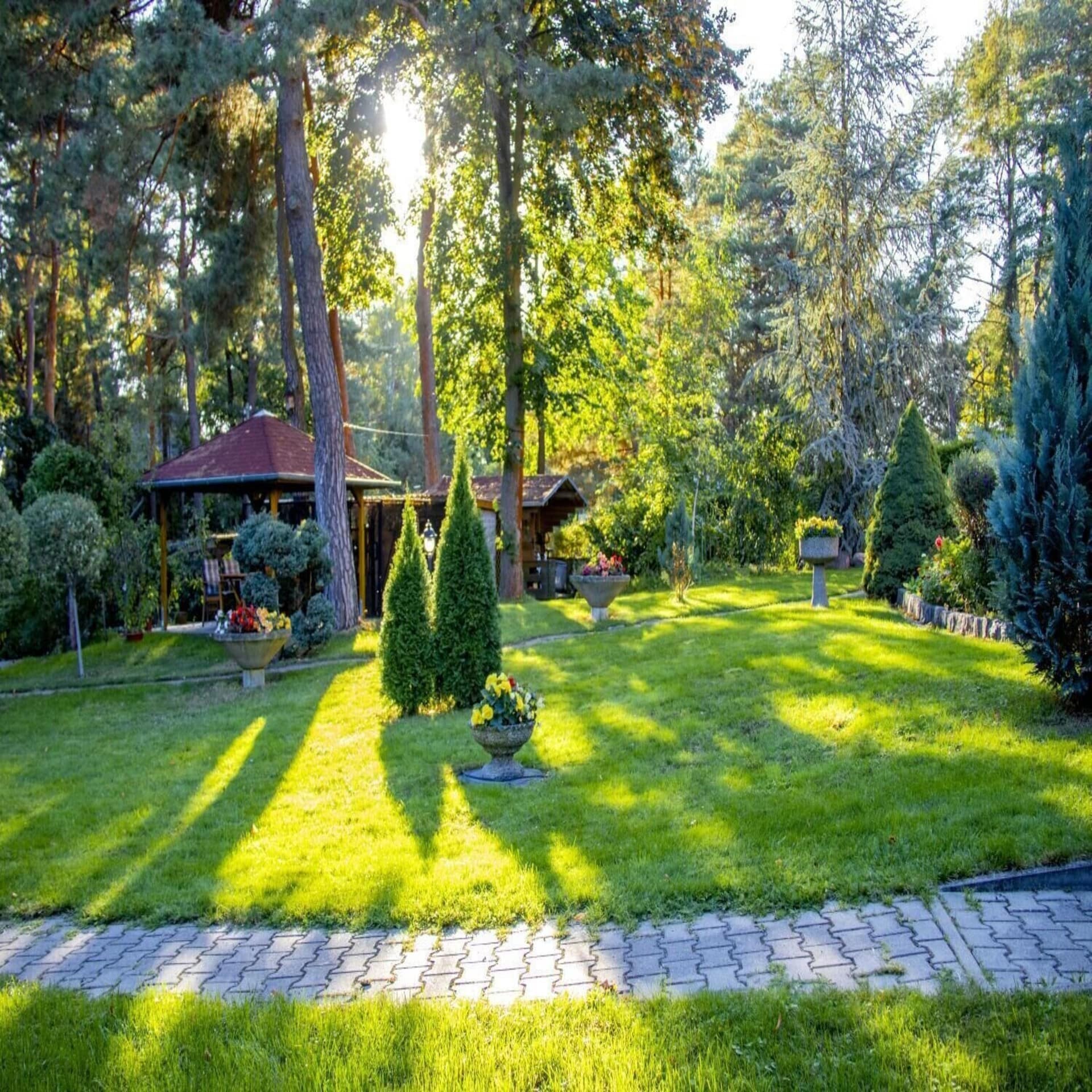 Weitläufiger grüner Garten mit kleinen Holzhäuschen. Die Sonne scheint durch die Bäume. 