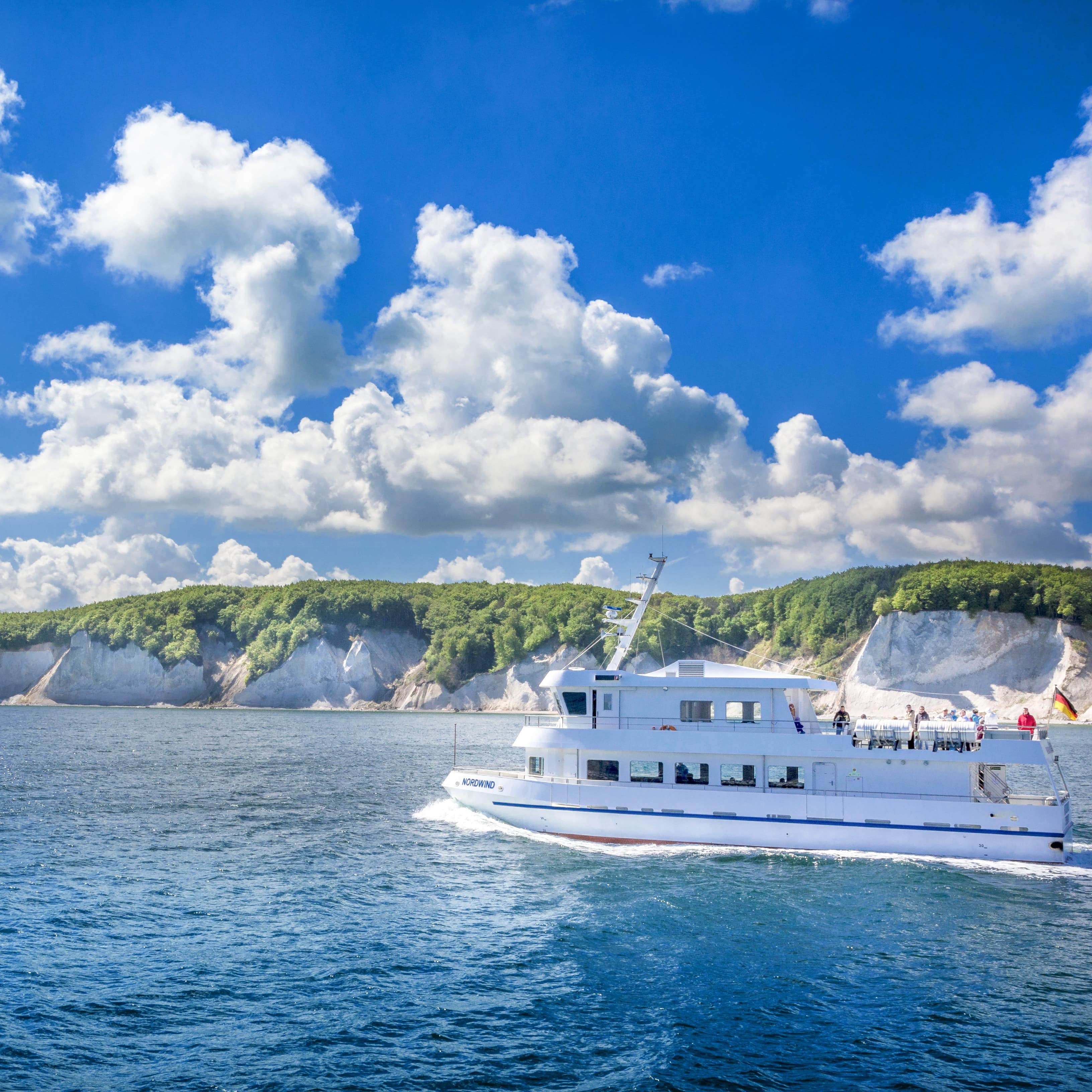 Ein weißes Ausflugsboot fährt vor den Kreidefelsen durchs Wasser.